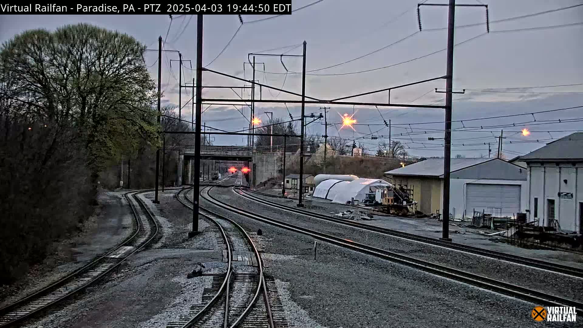Several sets of train tracks converge near some buildings under a twilight sky.