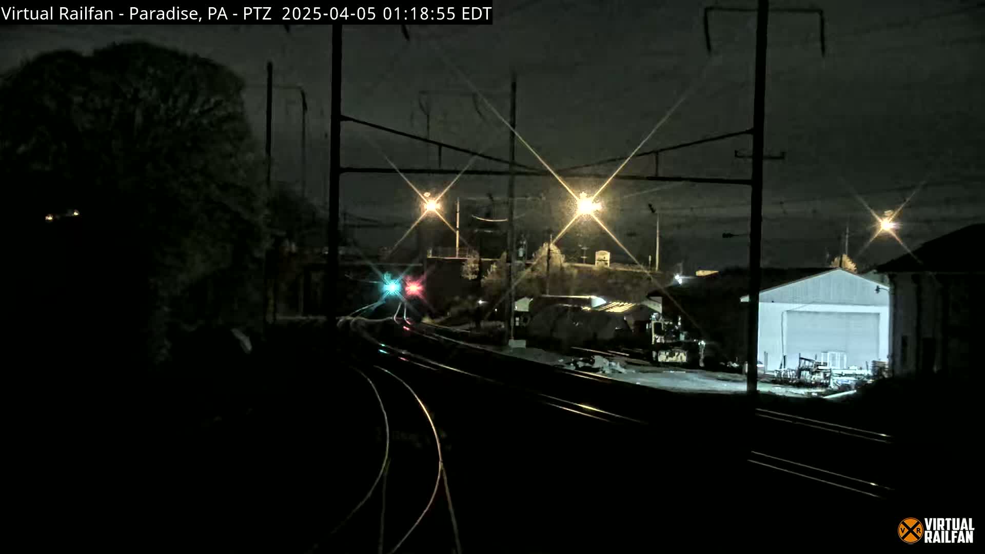 A nighttime view of railroad tracks and switching yards, illuminated by several lights, under a dark, clear sky.