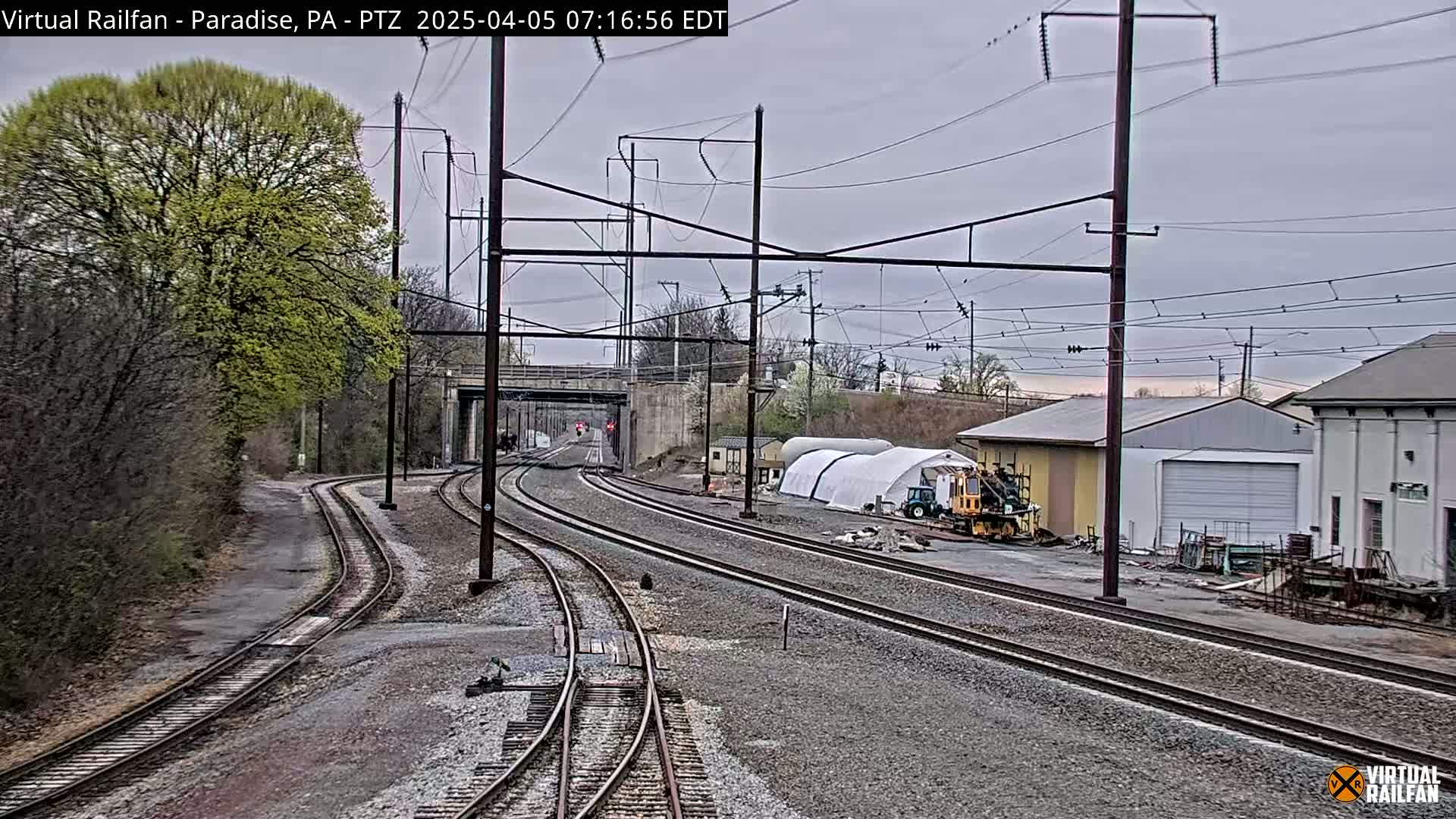 Multiple train tracks wind through a landscape of trees, buildings, and overcast skies.