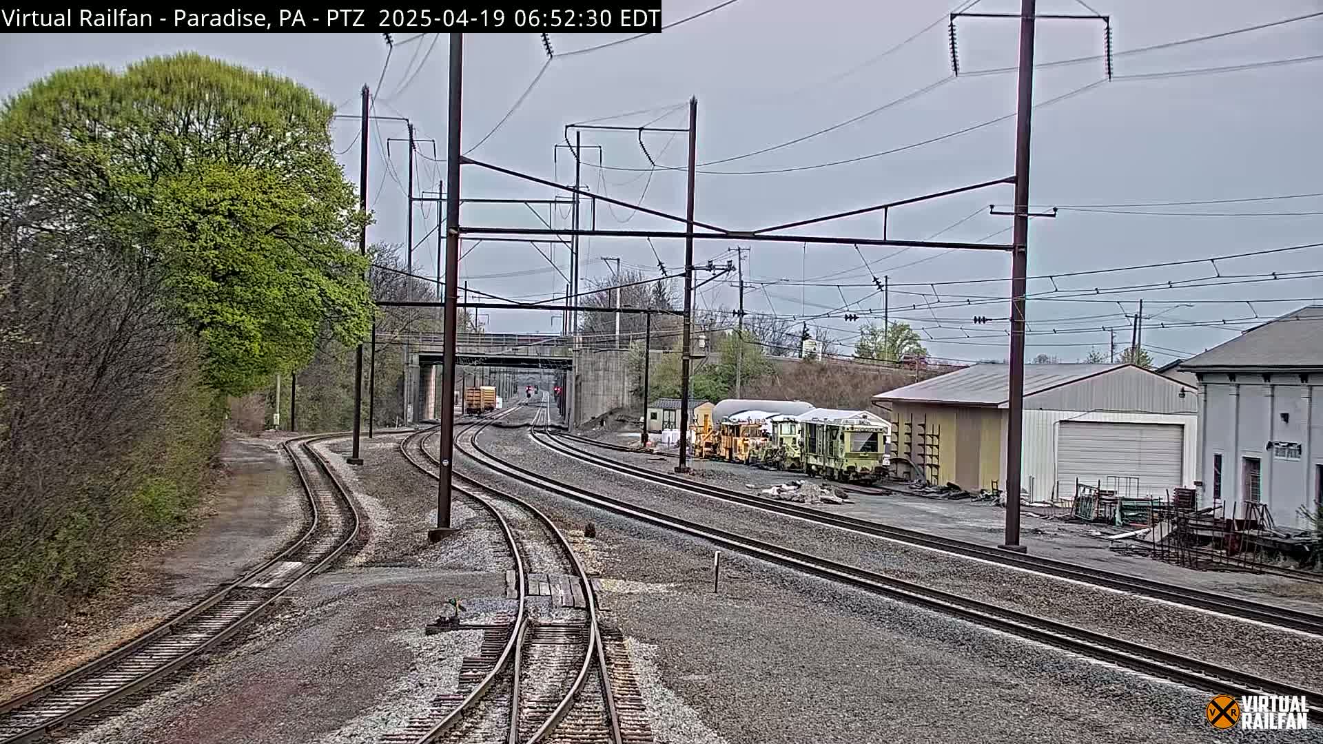 Multiple sets of train tracks curve through a landscape of trees and buildings under an overcast sky.