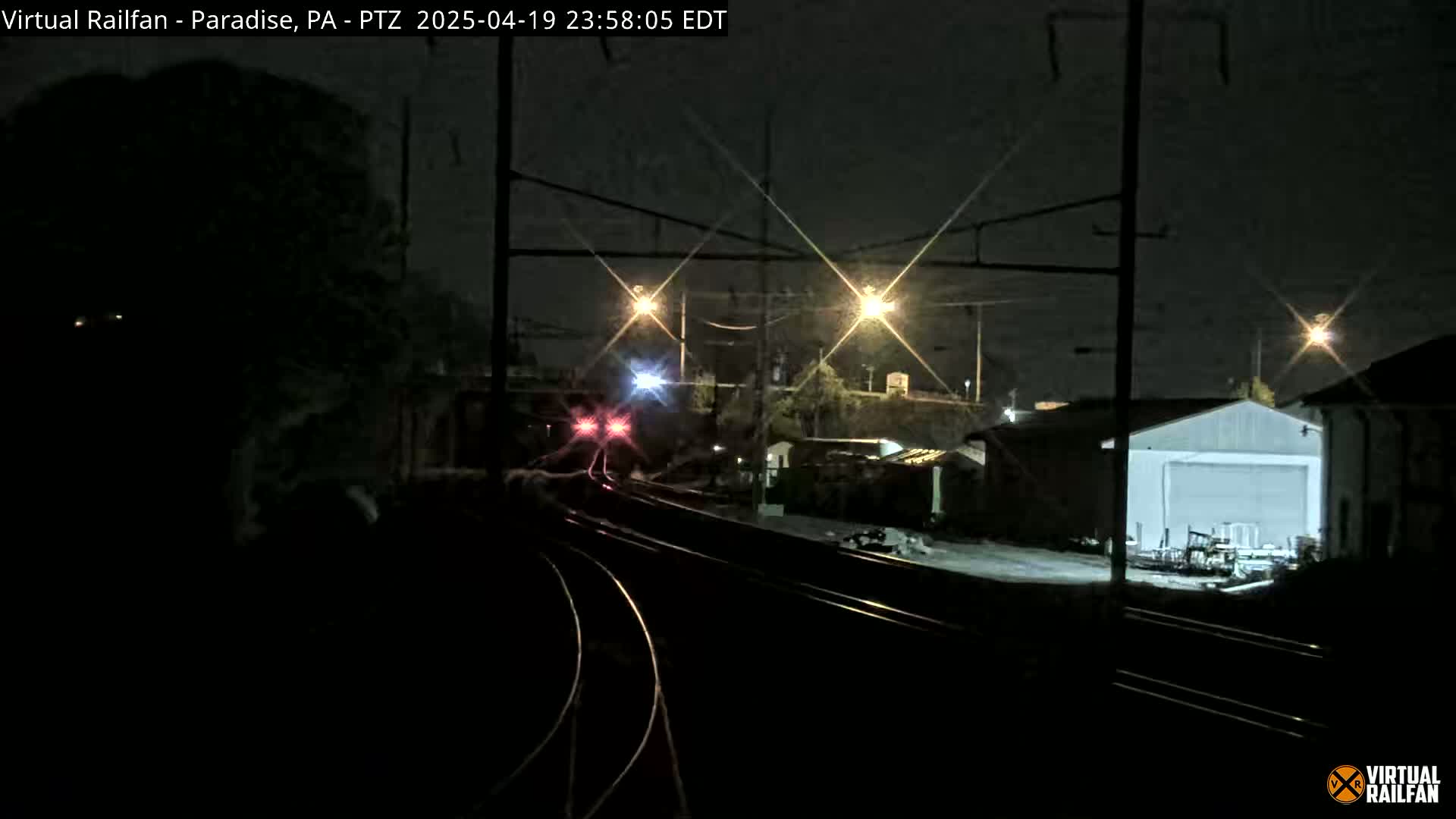 A nighttime view of a train approaching a railway station under artificial lighting.
