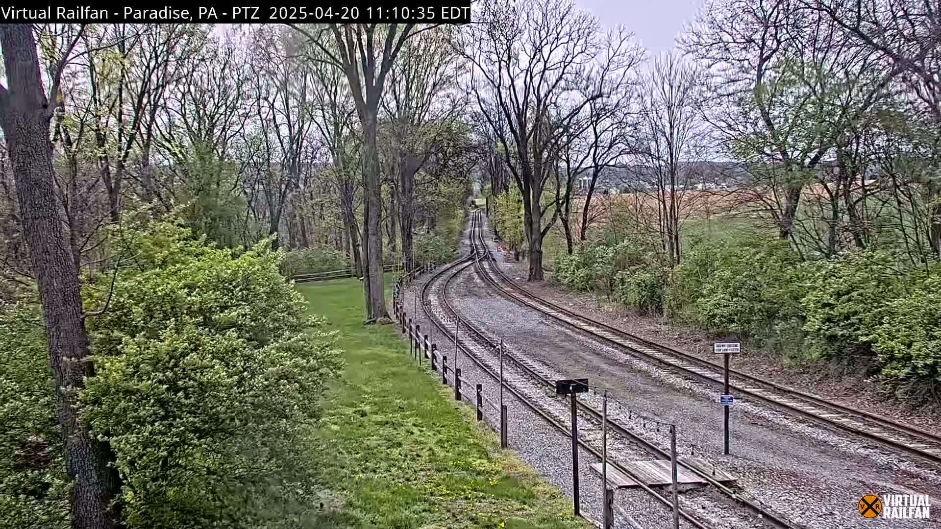 Railroad tracks curve gently through a tree-lined area on an overcast day.