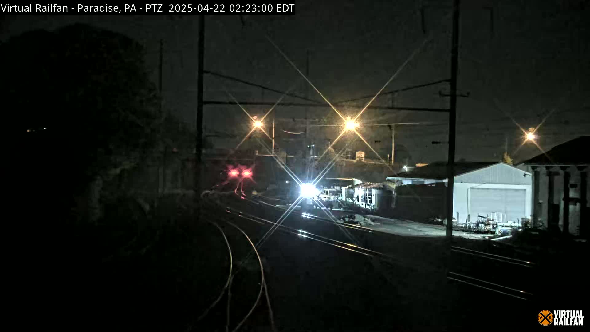 At night, a train passes by a railway under streetlights near some buildings.