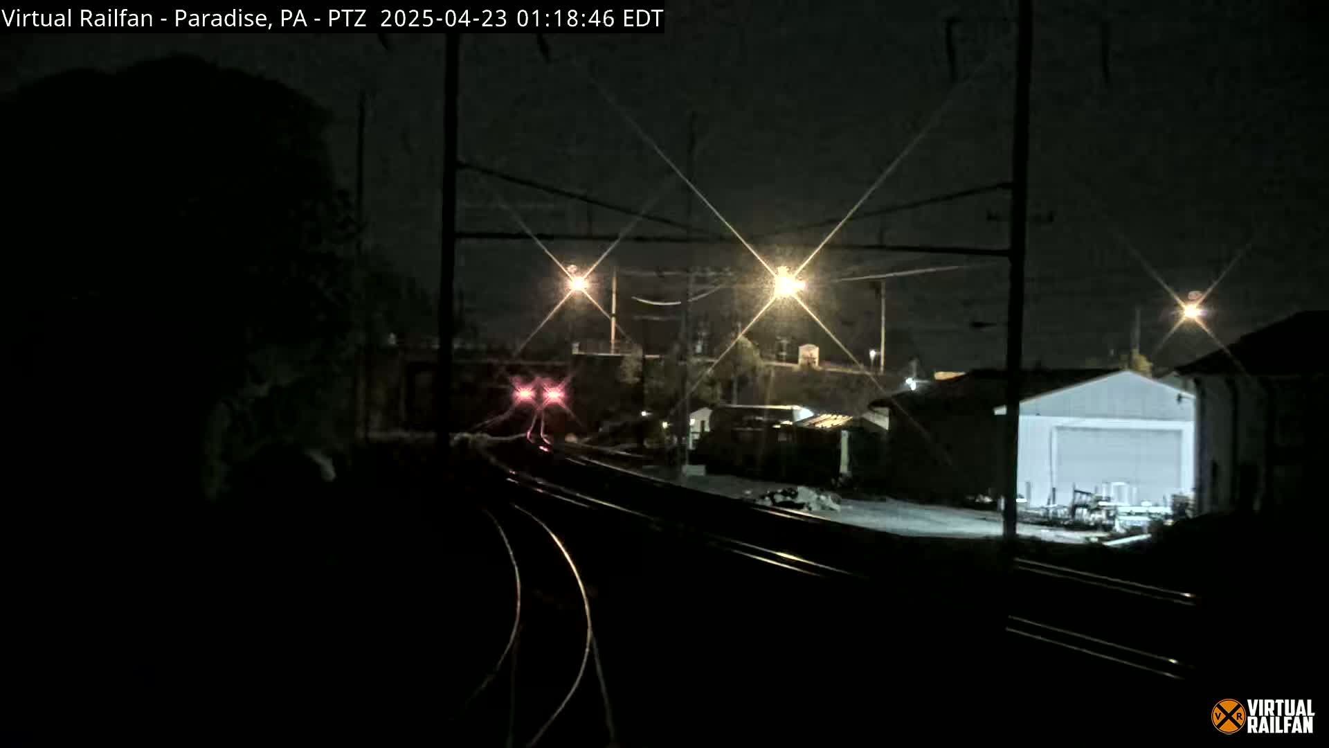 A nighttime view of a train approaching a railway station under clear skies, with several lights illuminating the scene.