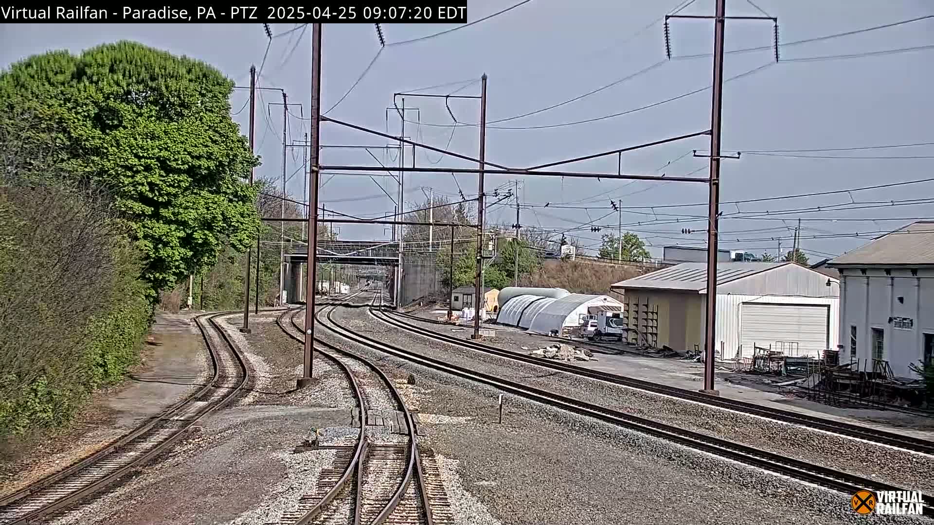 Multiple sets of train tracks curve toward a railway underpass on a partly sunny day.