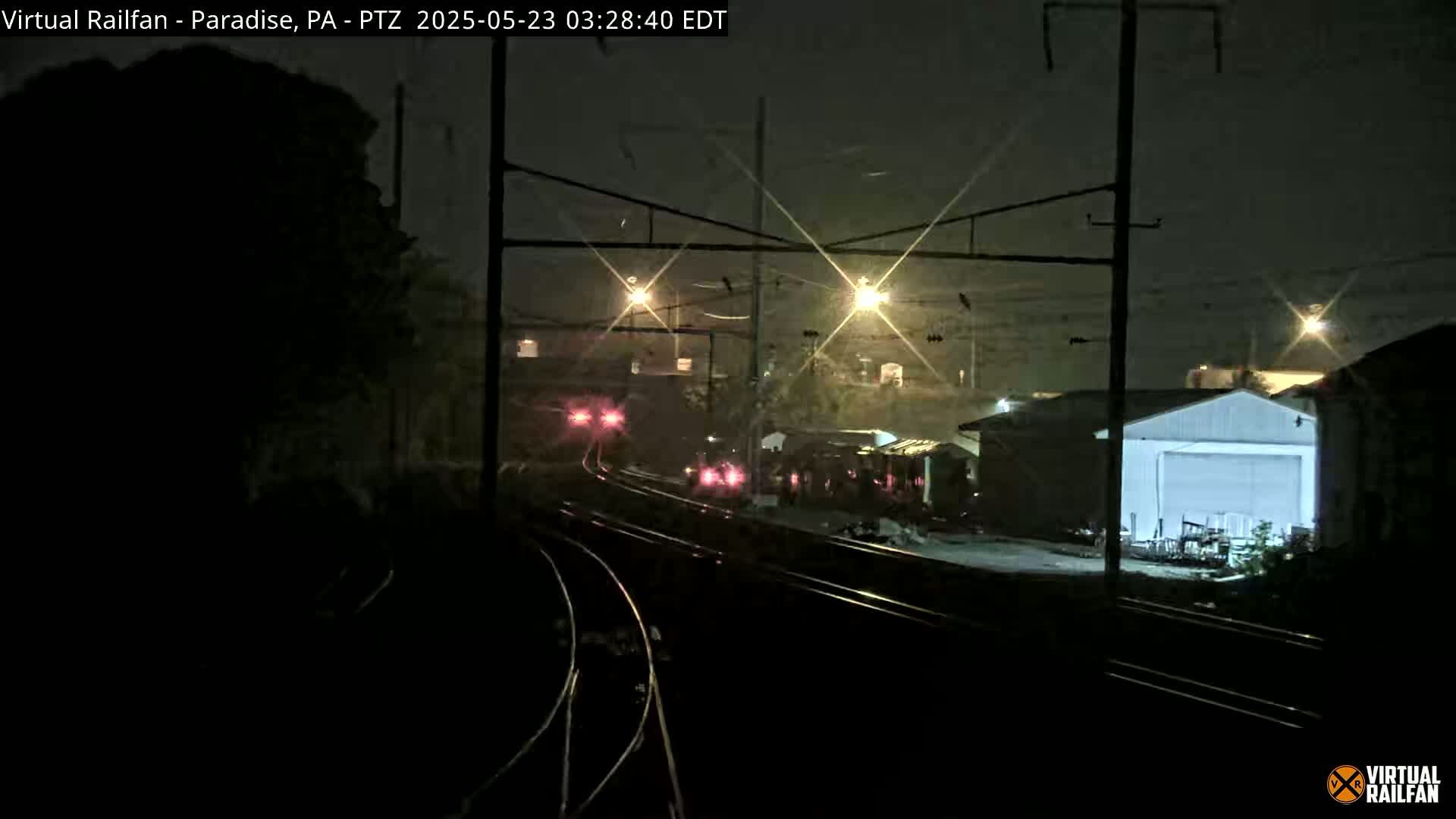 A nighttime view of a dimly lit train yard with a train in the distance under overcast skies.