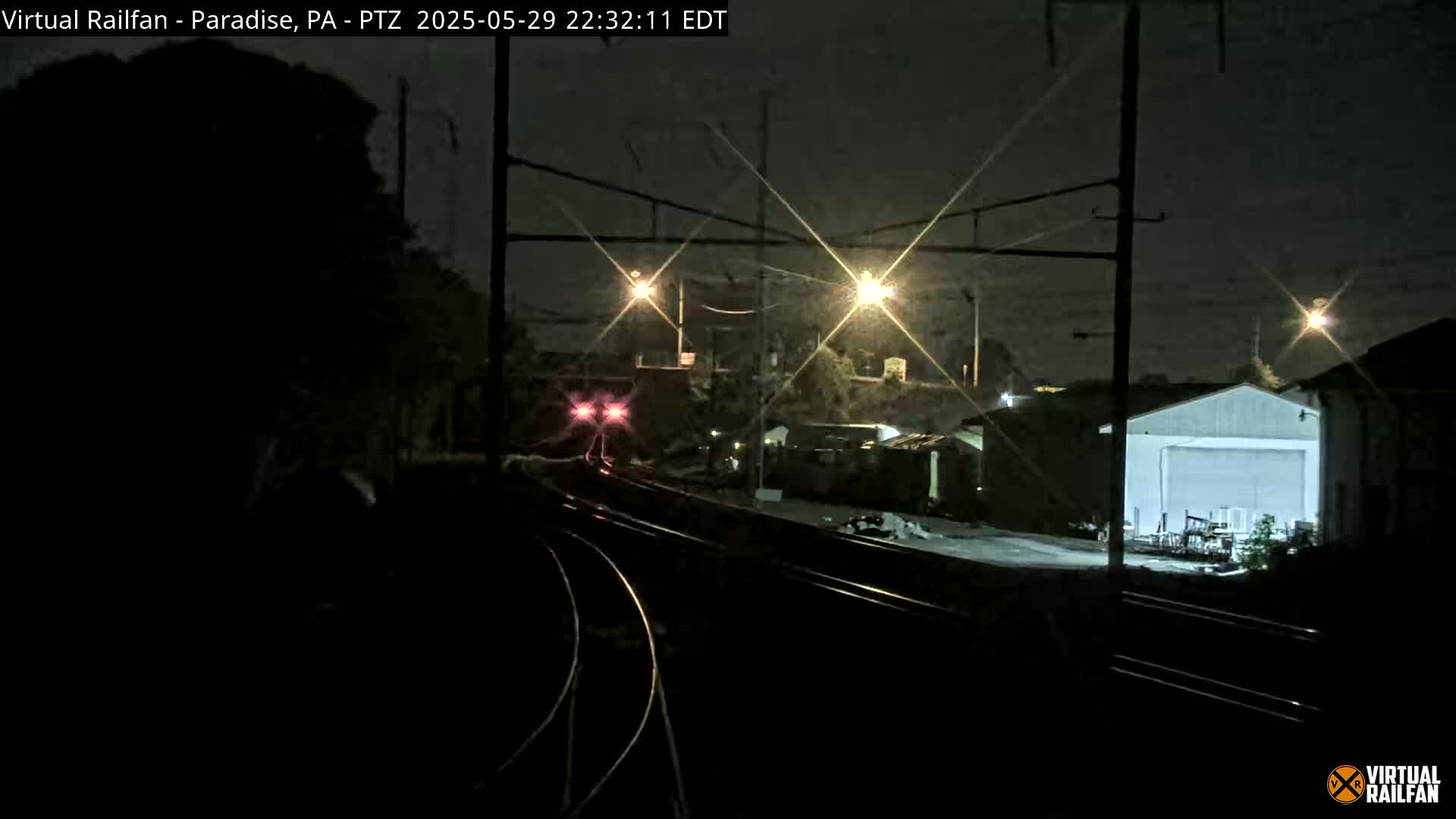 A nighttime view of a train approaching a rail yard under dark, clear skies, illuminated by artificial lights.
