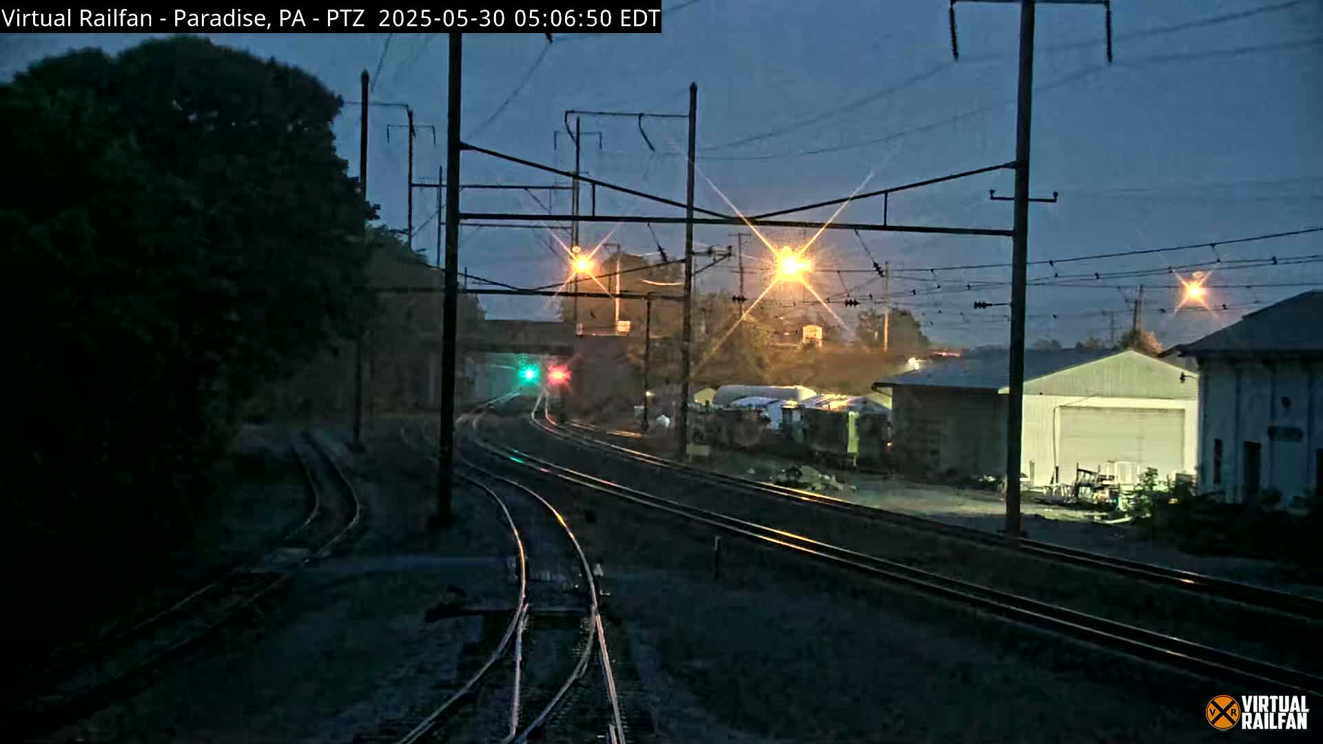 A nighttime view of railroad tracks, with a train visible in the distance under a dark, twilight sky.