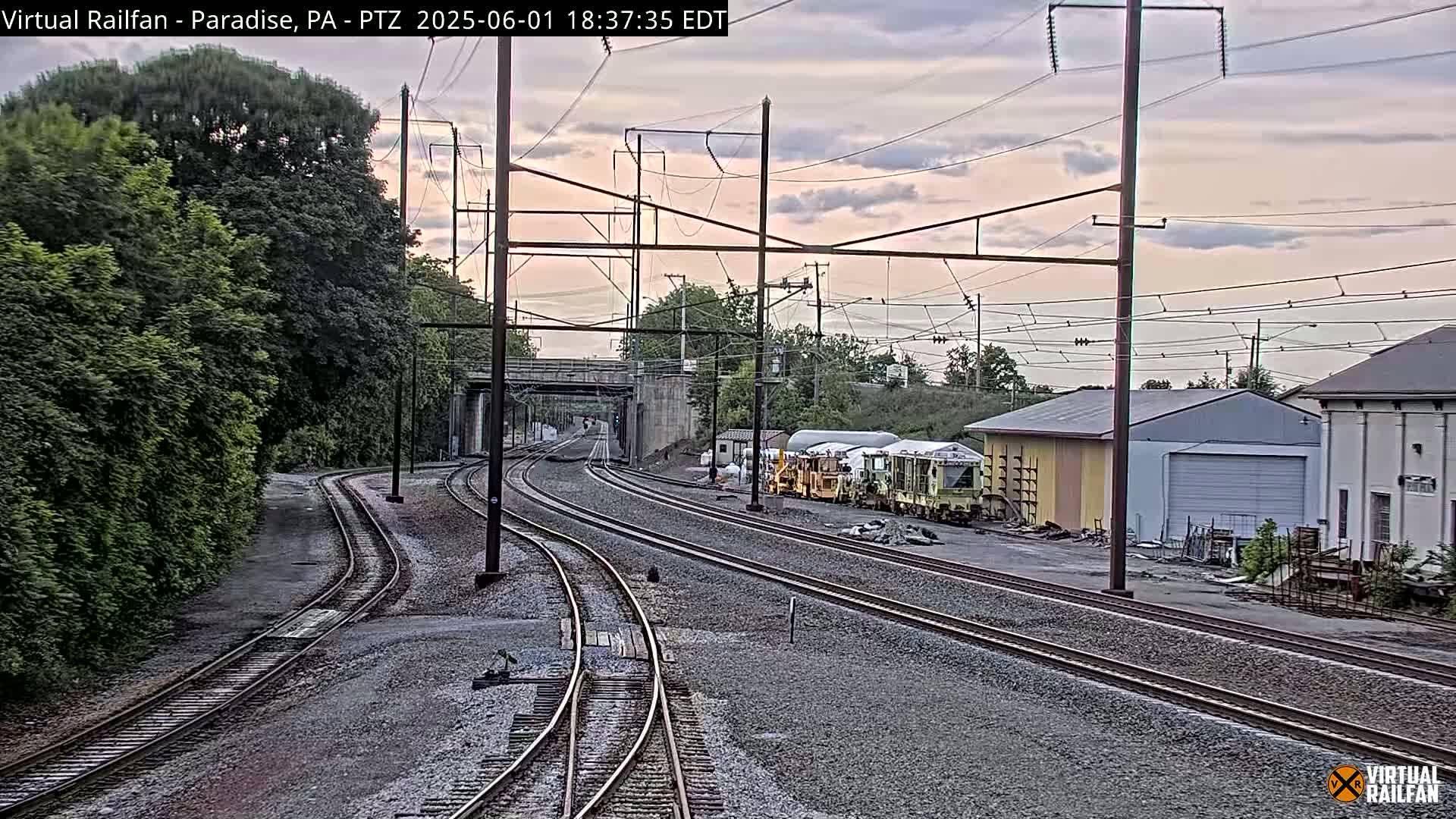 Several sets of train tracks converge near a railway yard under a partly cloudy evening sky.