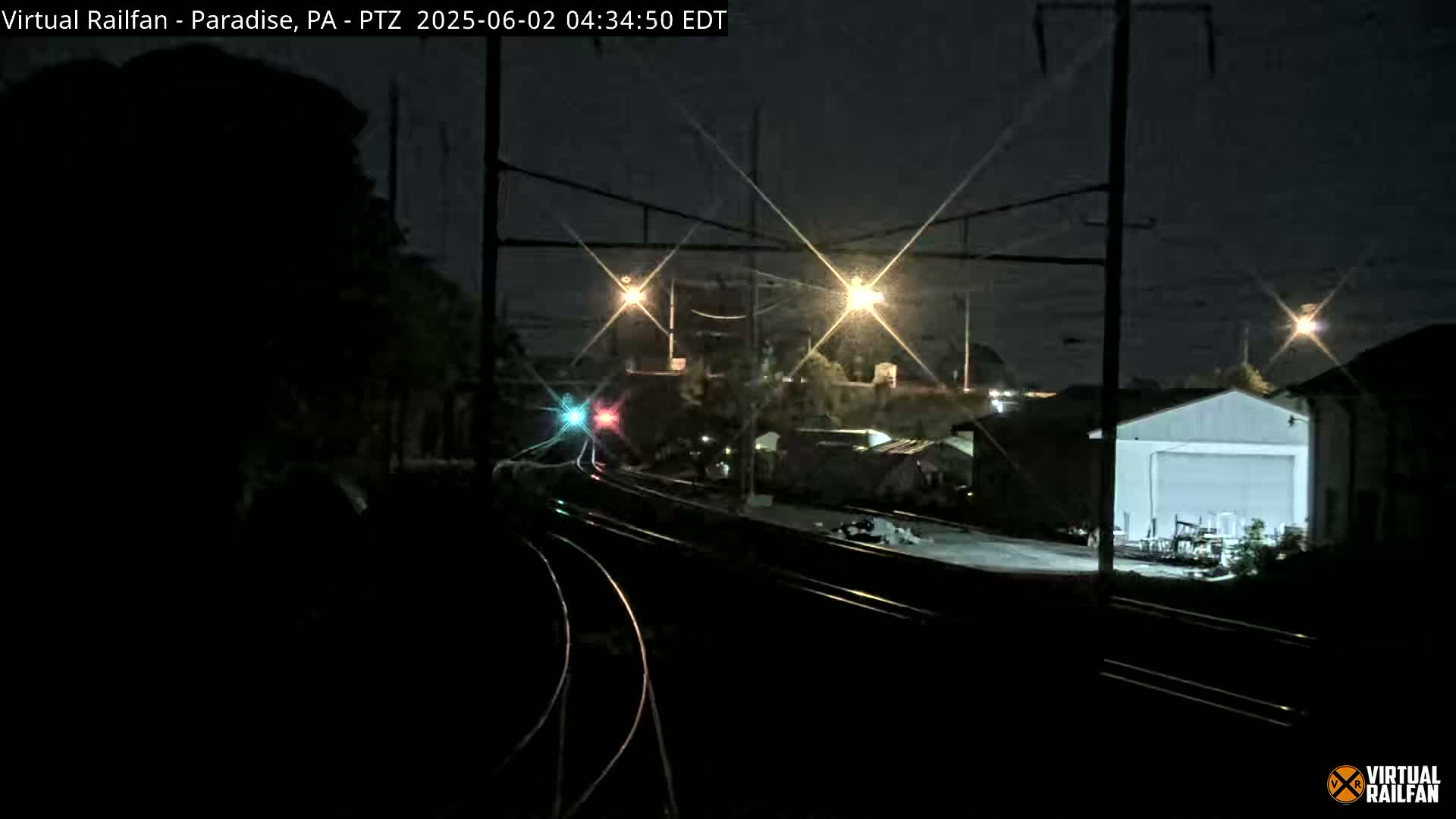 A nighttime view of railroad tracks and a building, illuminated by streetlights under a dark sky.