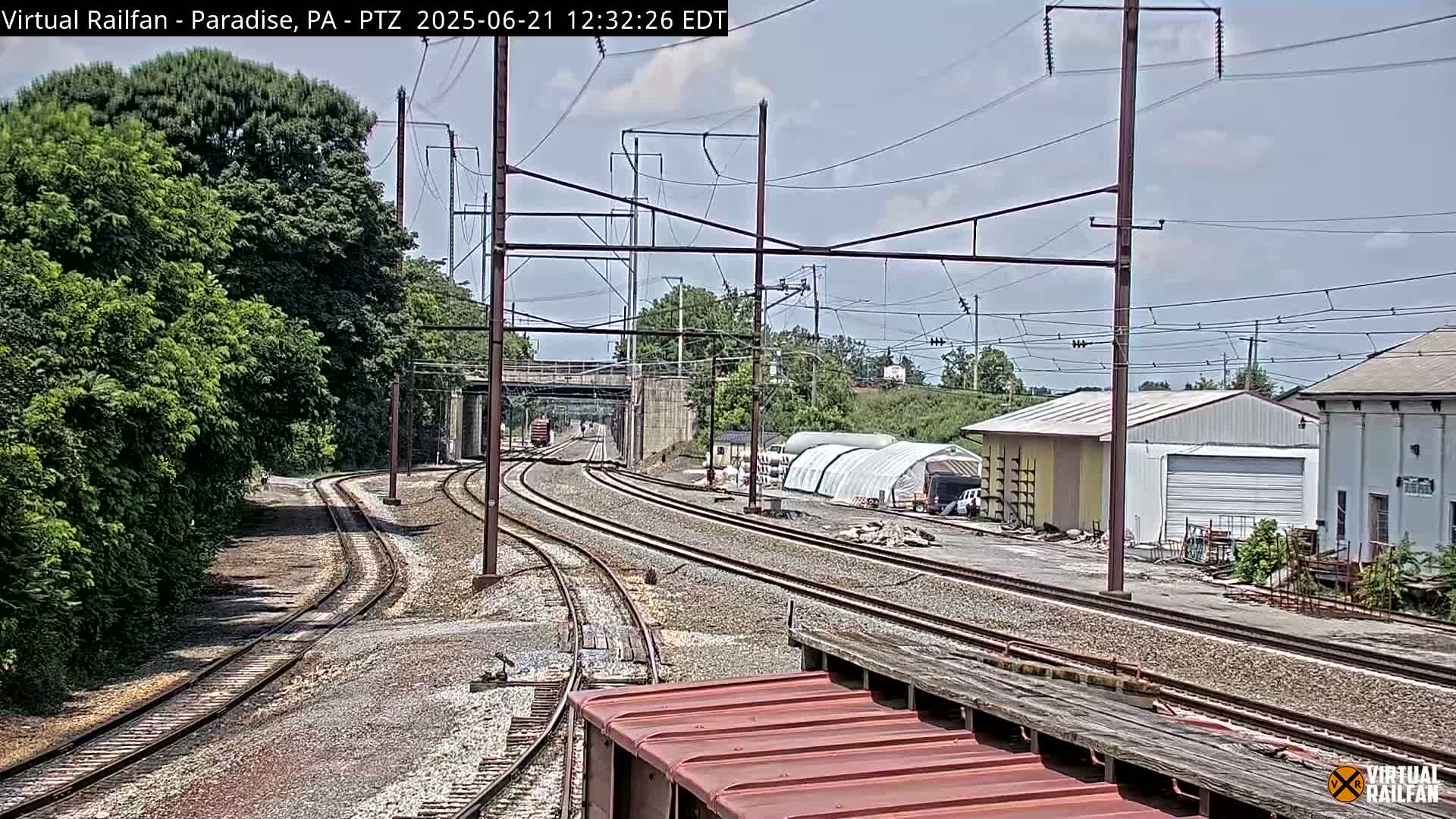Multiple train tracks diverge in a yard near some buildings under a mostly clear sky.