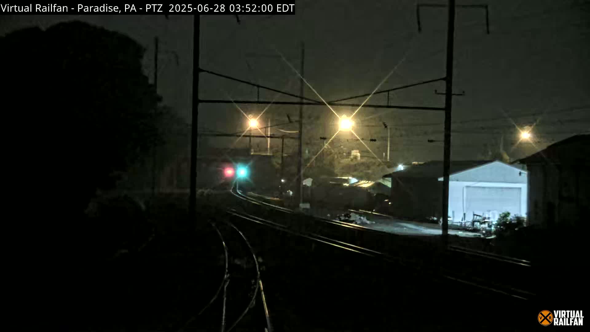 A nighttime view of railroad tracks and a nearby building, under hazy conditions.