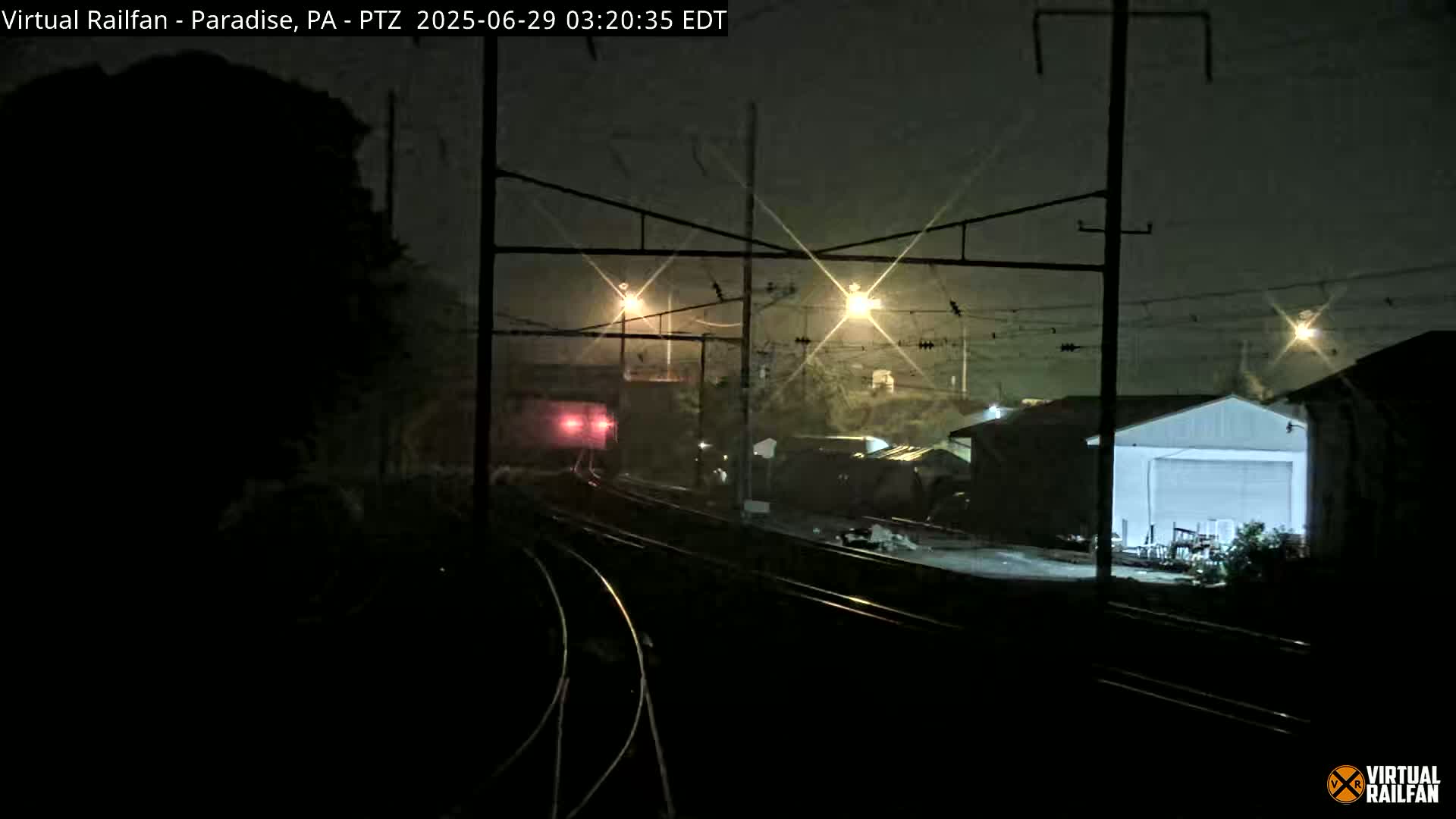 A train passes by industrial buildings at night in foggy conditions.