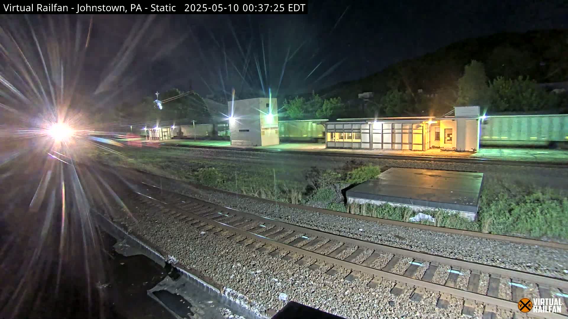 A train passes a nighttime railway station, its headlights creating a starburst effect.