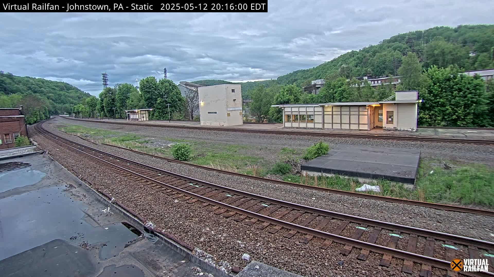 A train station with several buildings sits beside a curving railway track under an overcast sky.