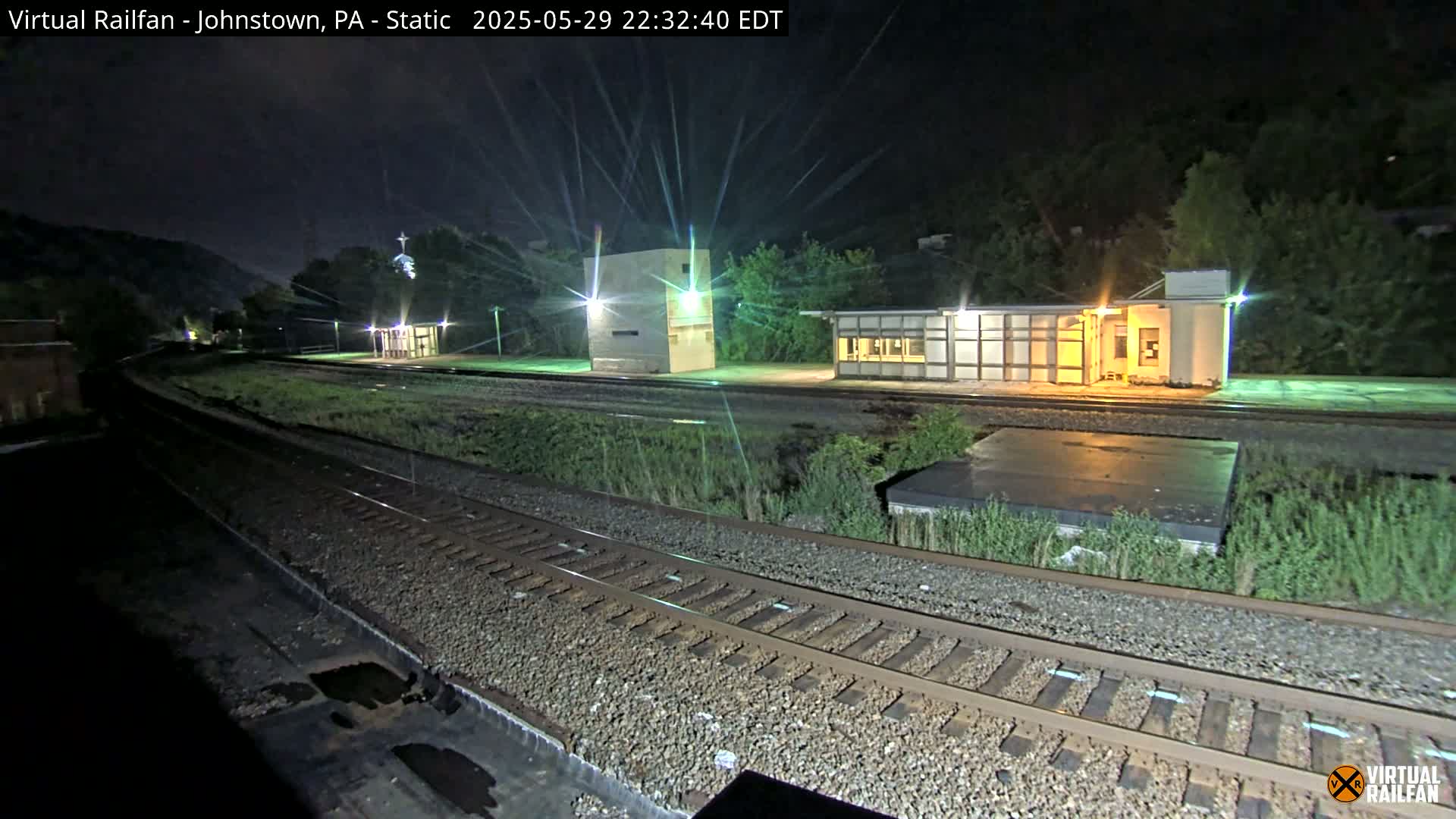 At night, a train station with several structures and train tracks is illuminated under a dark sky.