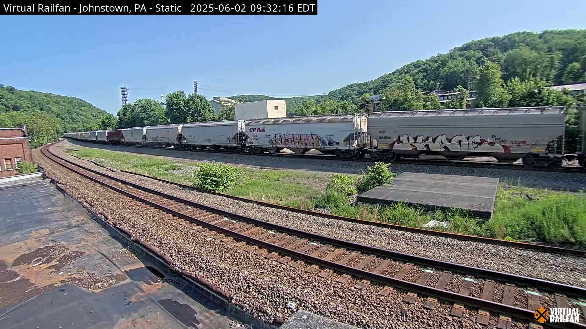 A long freight train, some cars of which are graffitied, is parked on a curving railway track under a clear blue sky.