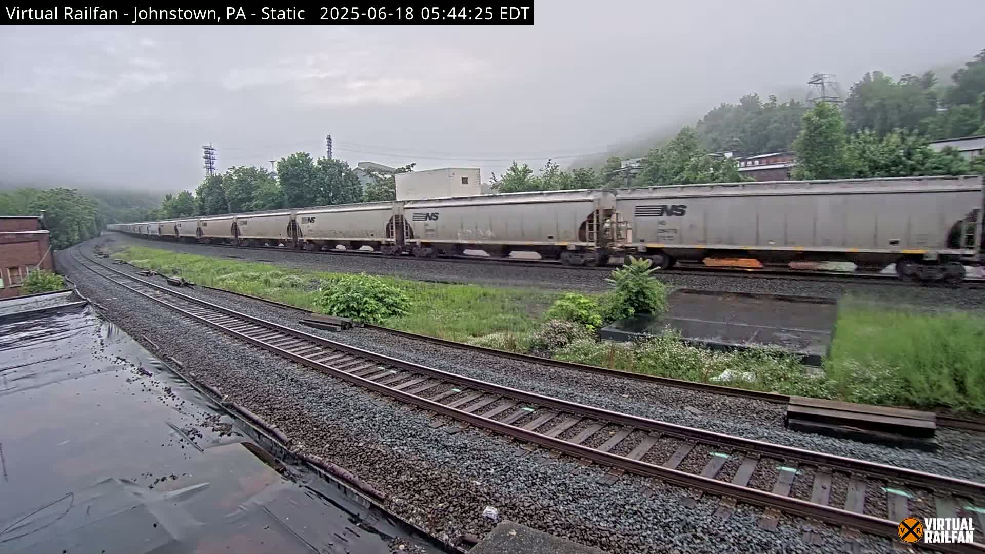 A long freight train curves around a bend on a railway track in foggy weather.