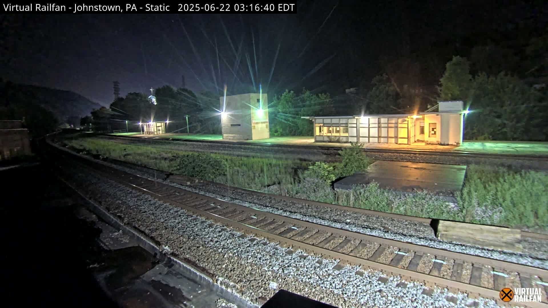 At night, a nighttime view of railroad tracks and several small buildings beside them, illuminated by artificial lights.