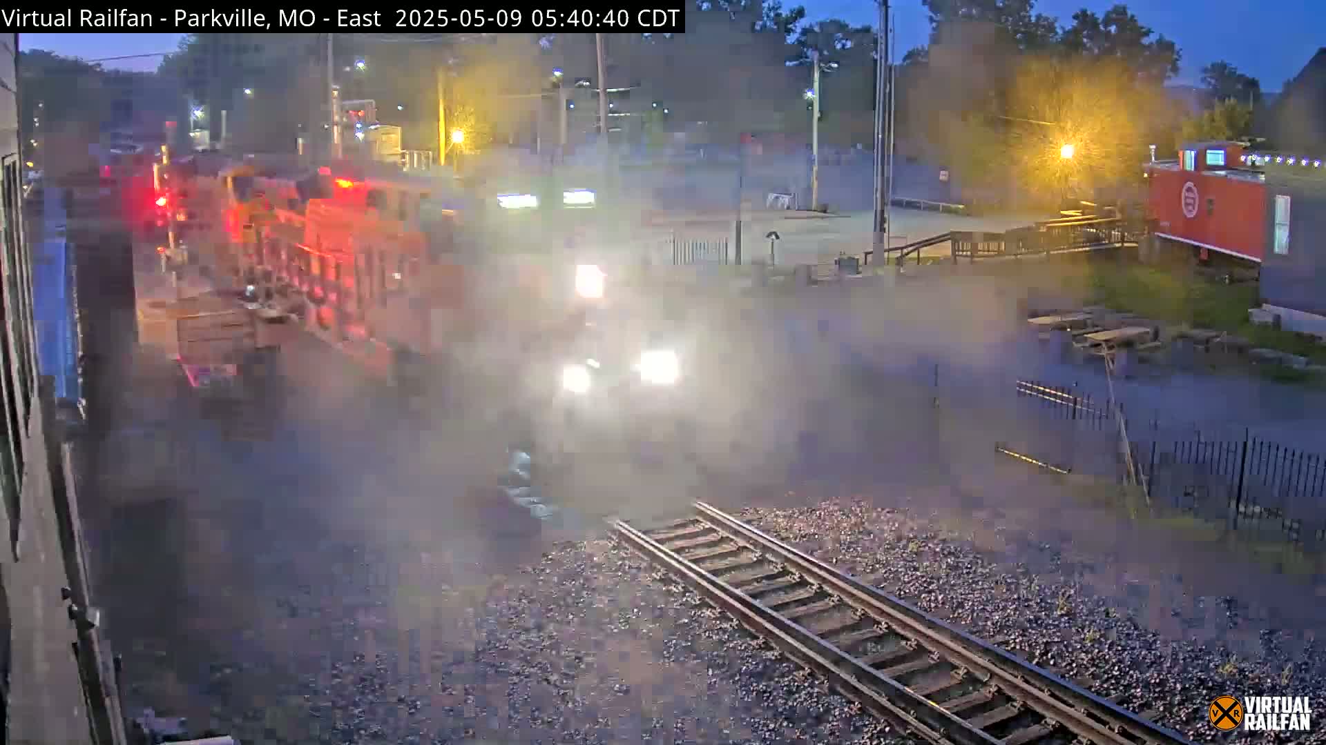 A train is moving through a dimly lit area at night, with a misty or foggy atmosphere present.