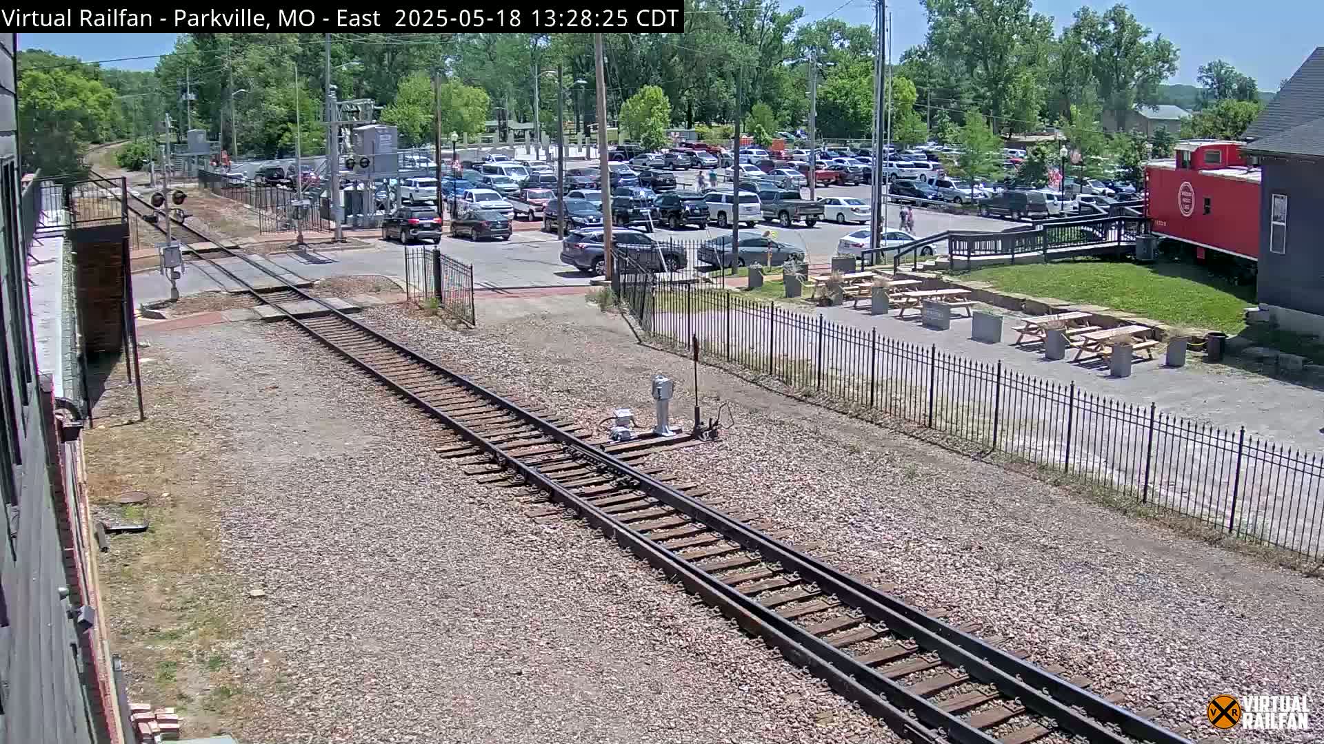A sunny day view of railroad tracks intersecting with a road next to a parking lot and a red caboose.