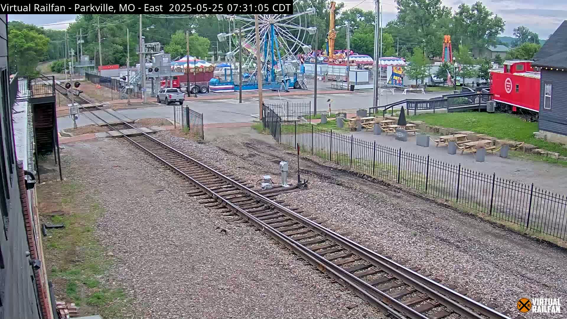 A view down a set of railroad tracks on an overcast day, with a carnival visible in the background.
