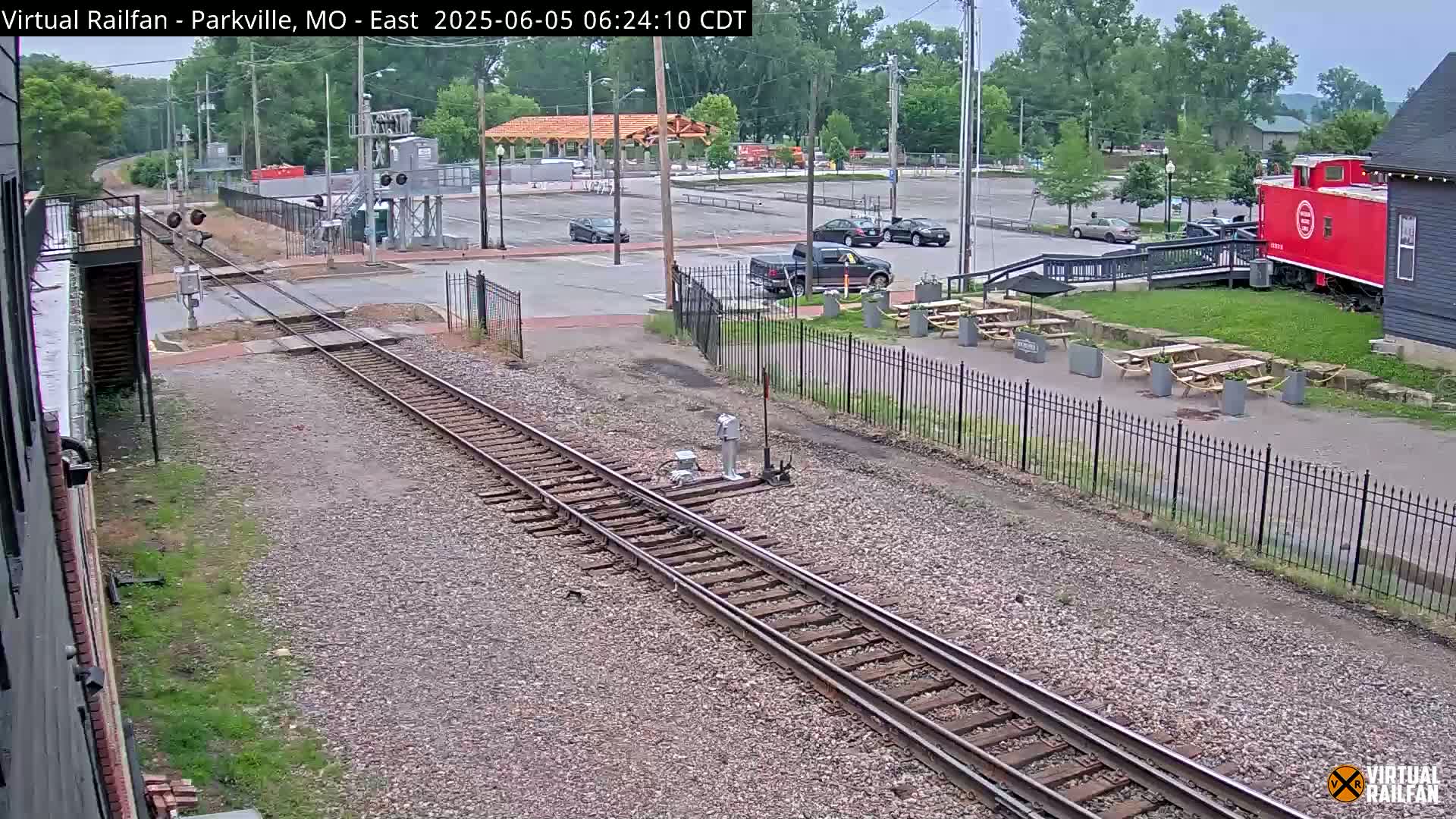 Railroad tracks and a red caboose are visible in a mostly empty parking lot on an overcast day.
