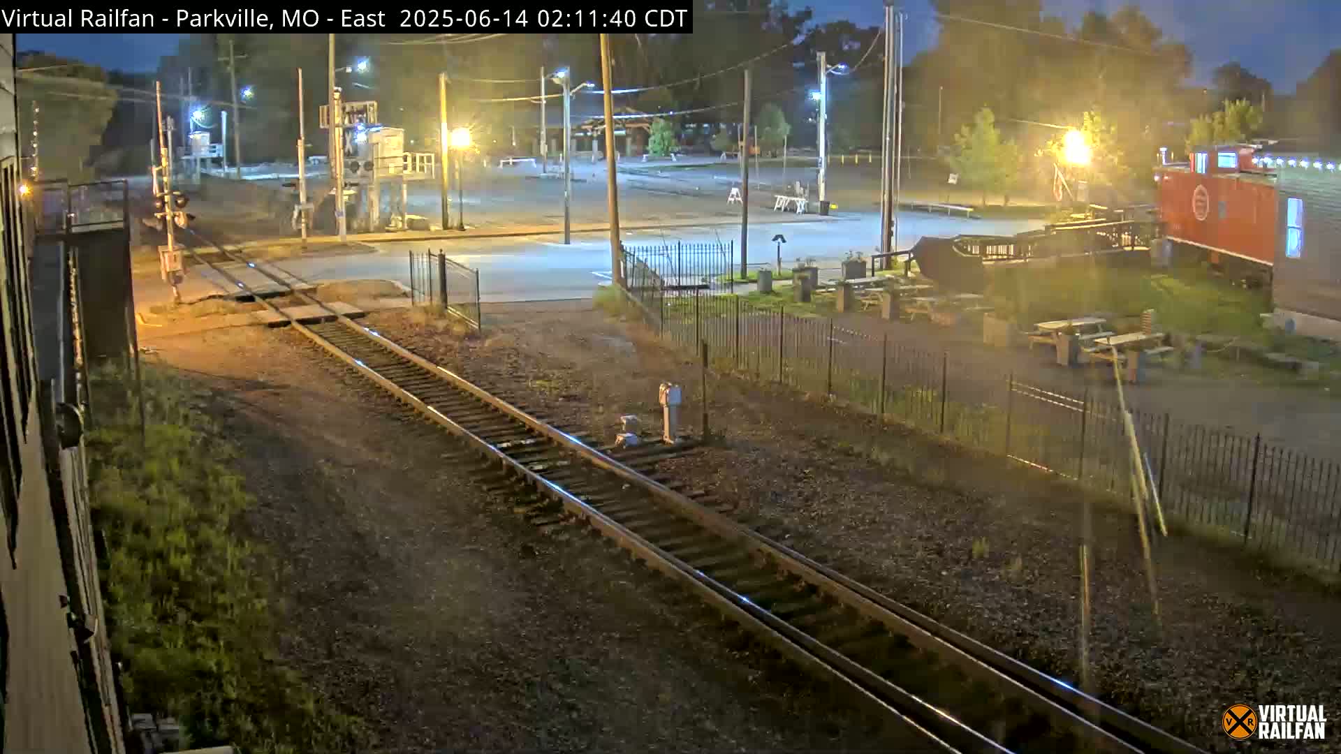 A nighttime view of a railroad crossing near a building with outdoor seating, under dark, clear skies.