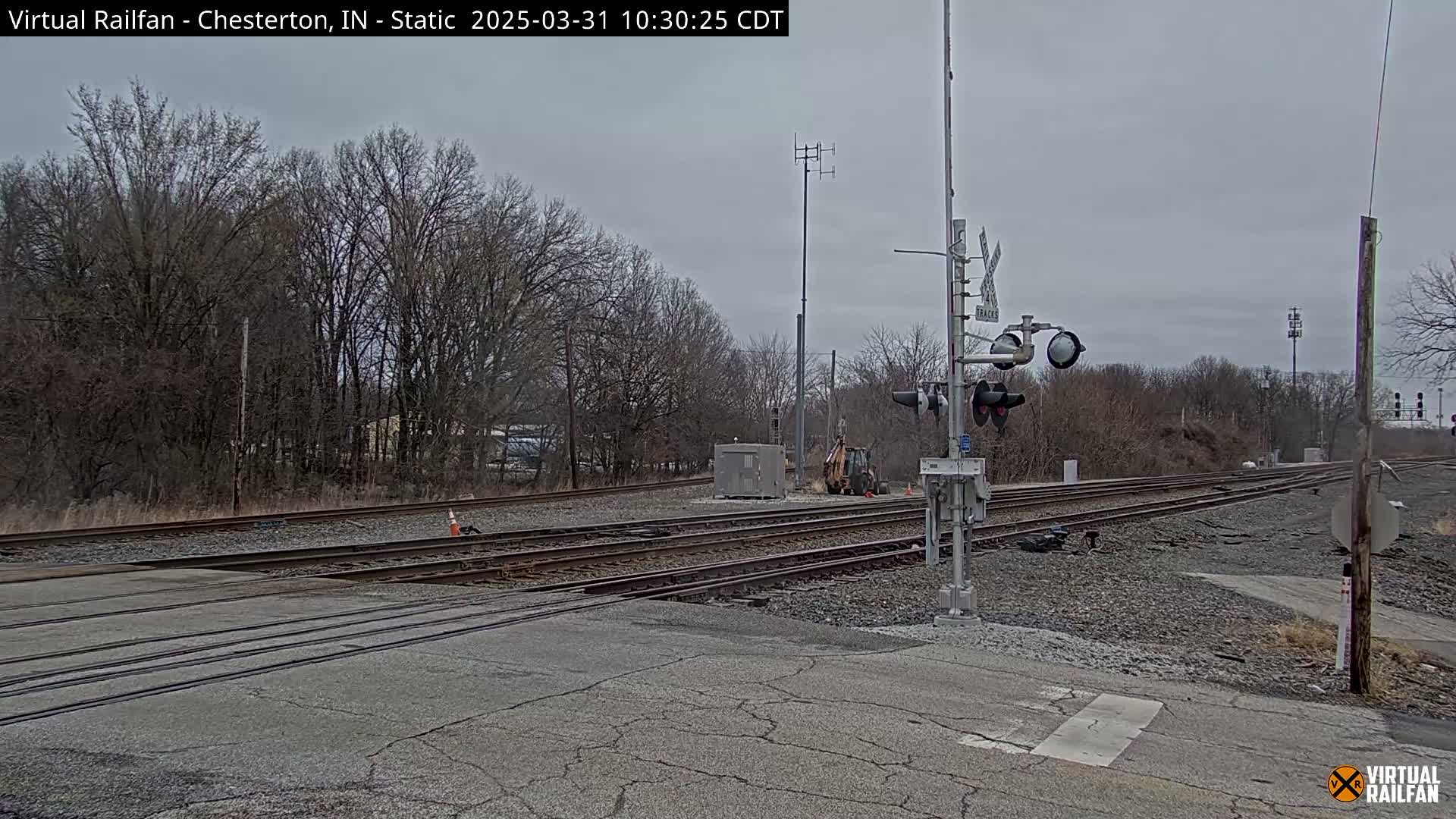 A railroad crossing with multiple tracks, under an overcast sky, is surrounded by bare trees.