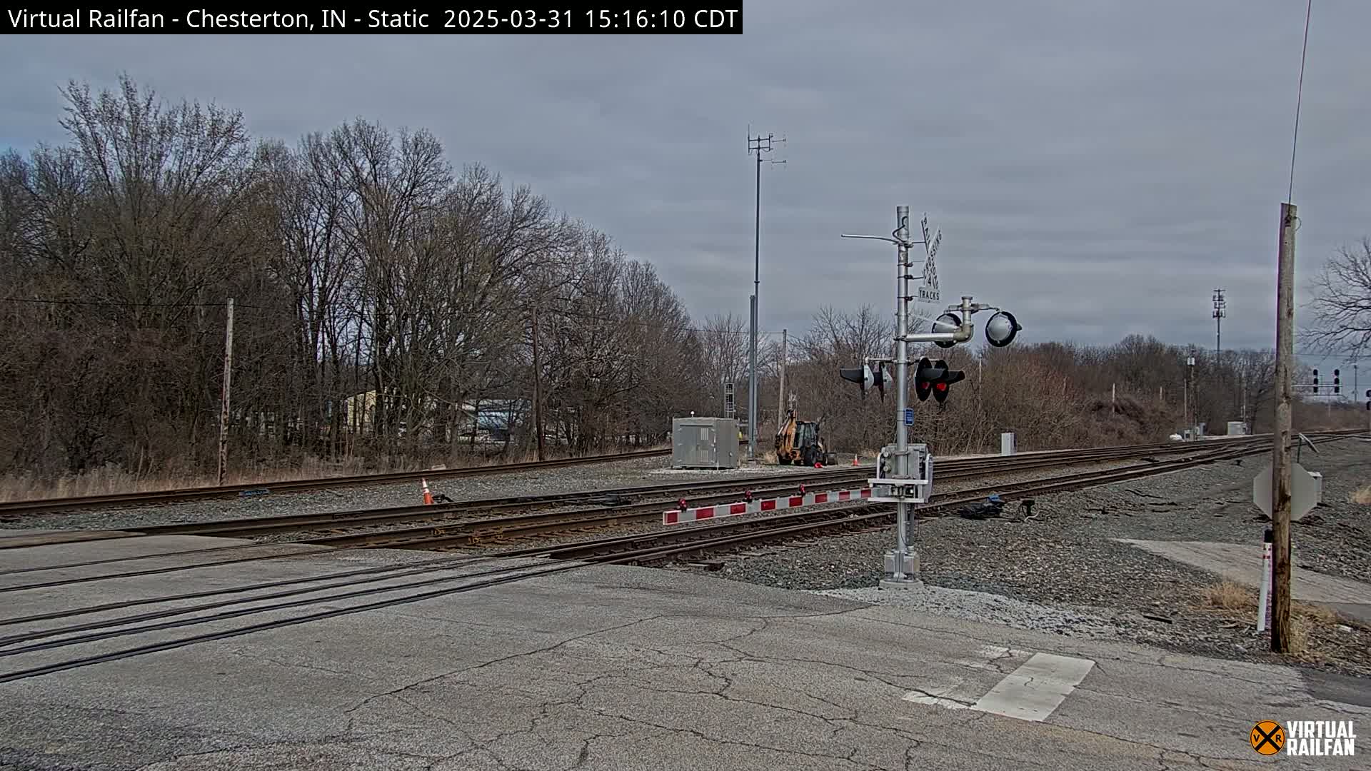 A railroad crossing with train signals and bare trees under an overcast sky.