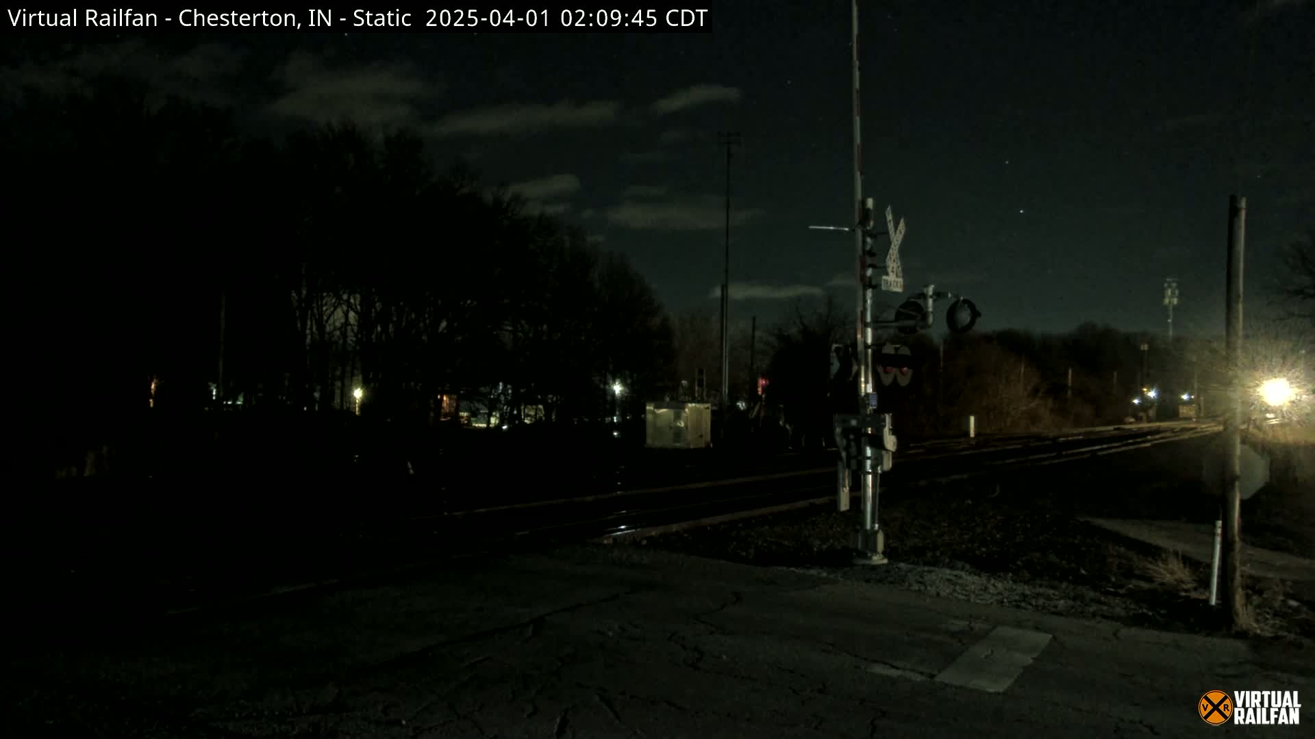 A nighttime view of a railroad crossing with a signal, under a partly cloudy sky.