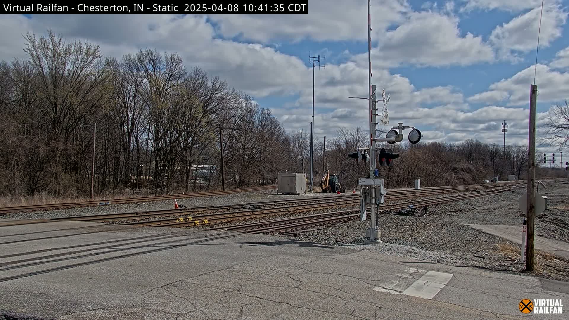A railroad crossing with several sets of tracks under a partly cloudy sky.