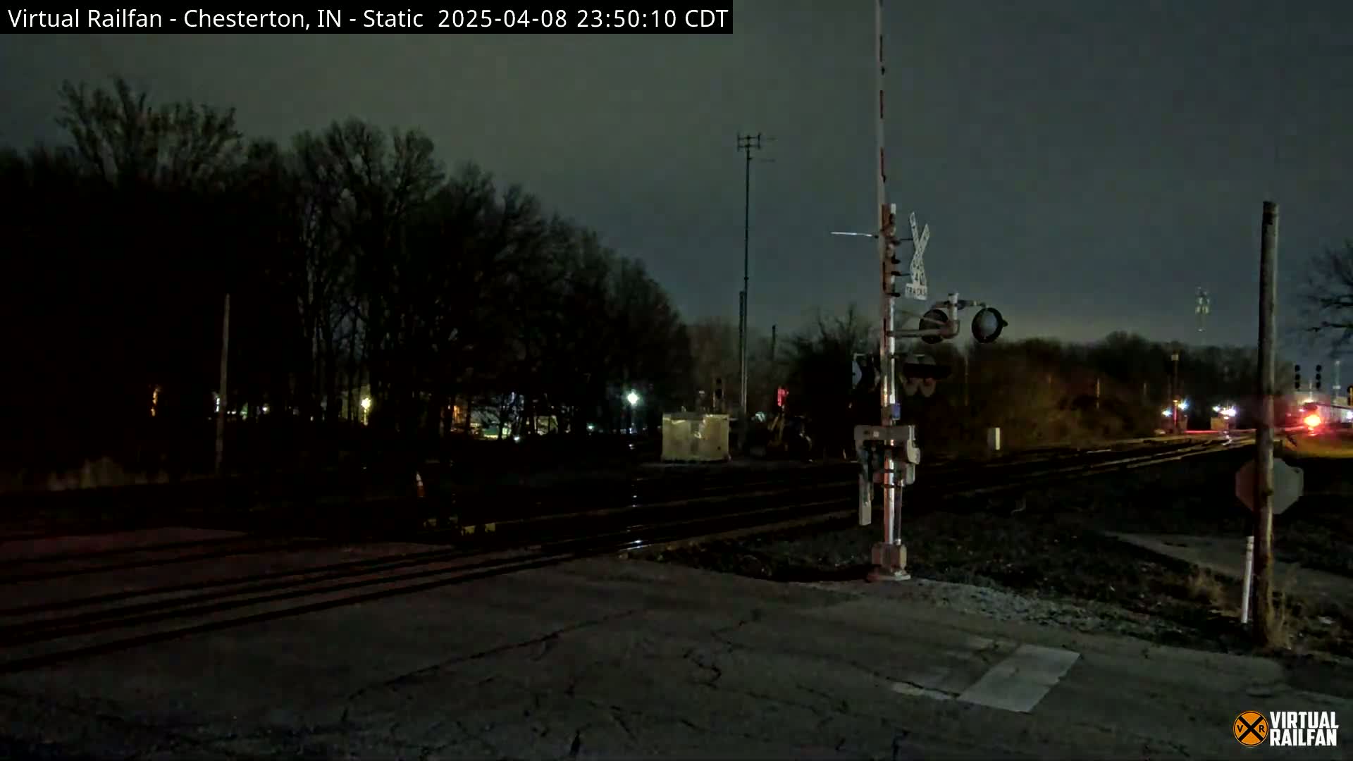 A nighttime view of a railroad crossing with a train in the distance under a dark sky.