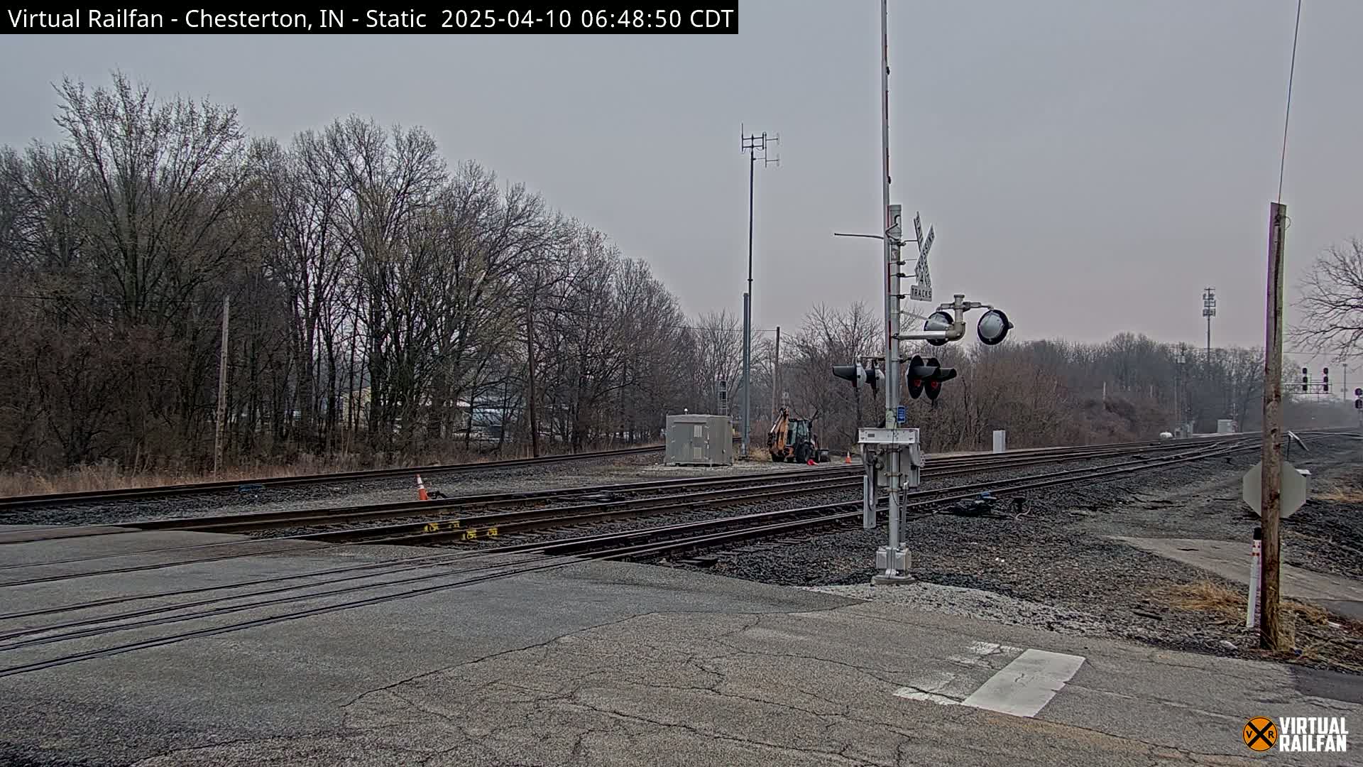 A railroad crossing with several train tracks, signal lights, and bare trees under an overcast sky.