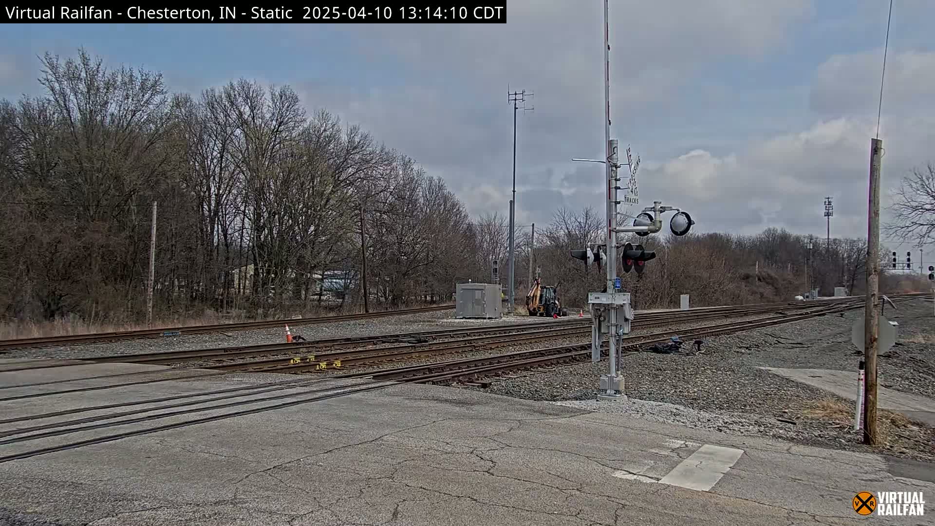 A railroad crossing with several tracks and a small piece of construction equipment is visible under a partly cloudy sky.