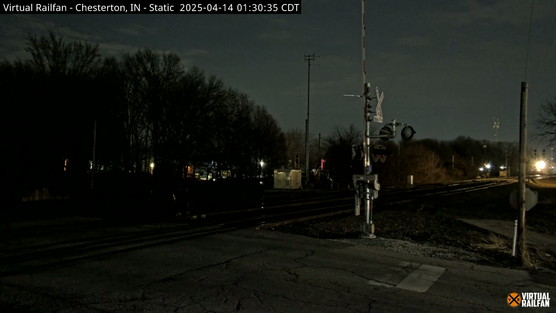 A nighttime view of a railroad crossing with train signals and tracks under a dark sky.