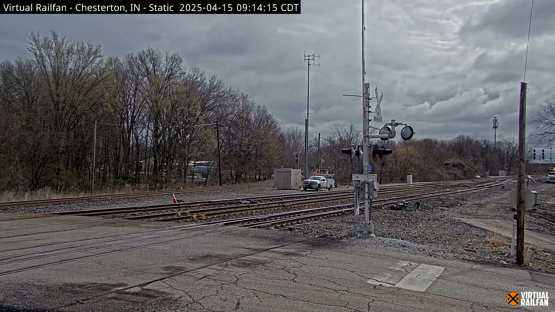 A mostly cloudy day shows a railroad crossing with a white pickup truck and a small utility vehicle near a set of railroad tracks that intersect a road.