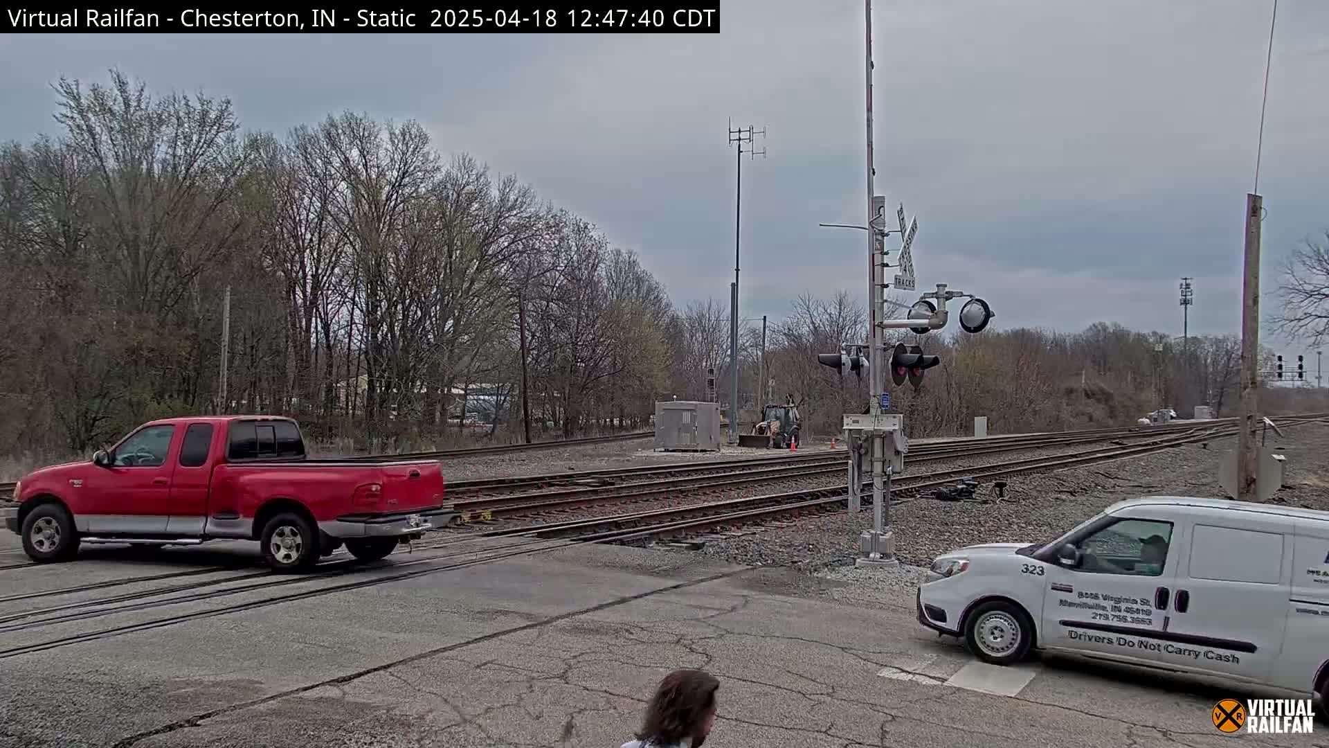 A red pickup truck and a white van are stopped near railroad tracks under an overcast sky.