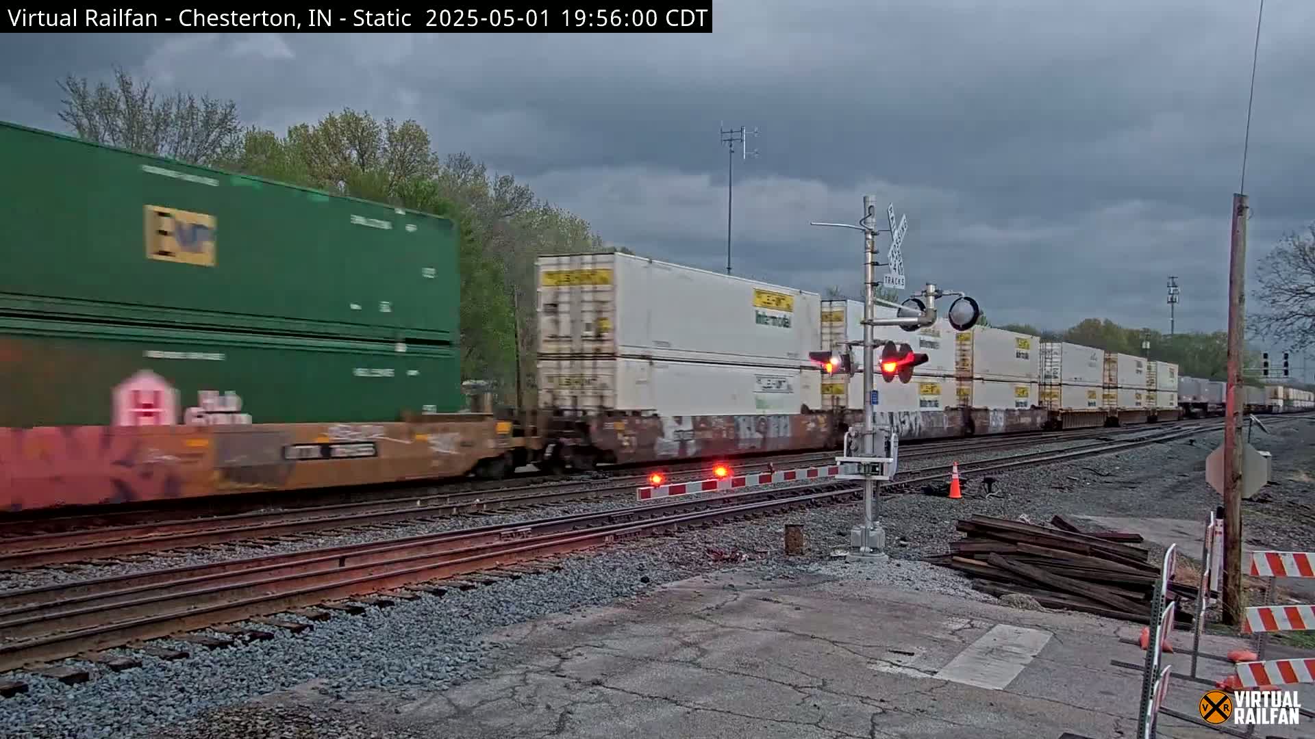 A long freight train with various colored shipping containers passes a railroad crossing under an overcast sky.