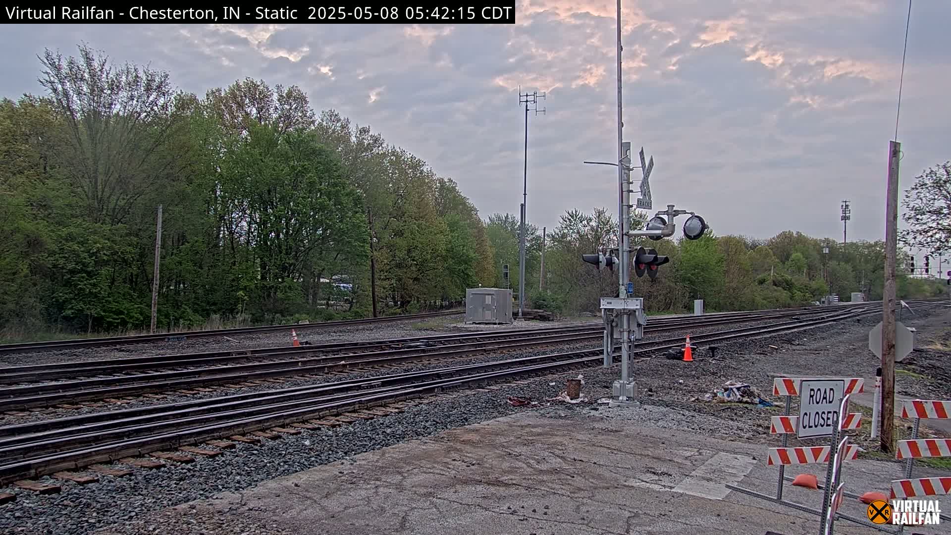 Multiple train tracks stretch into a wooded area under a partly cloudy sky.