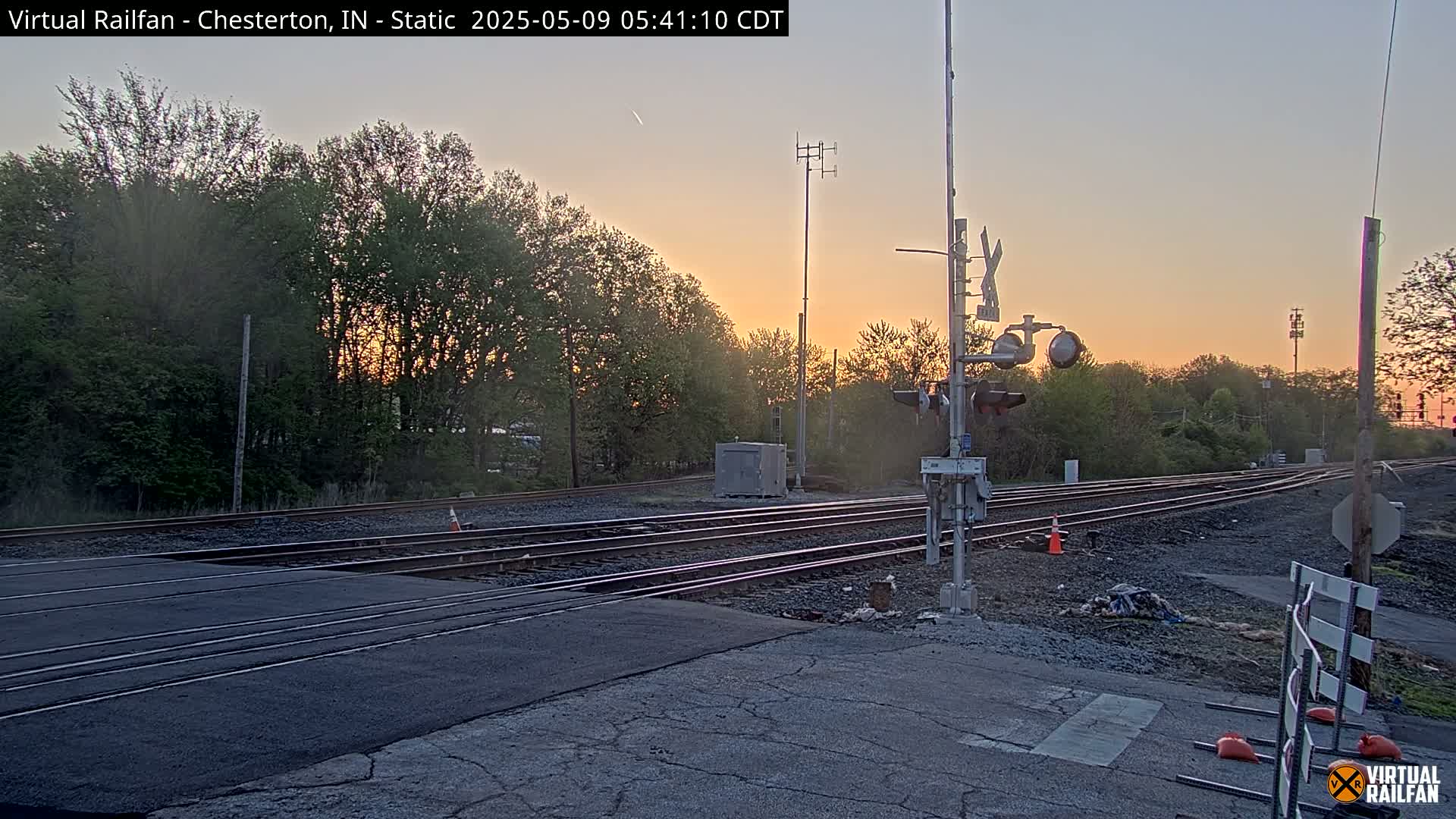 A railroad crossing at sunset, with multiple train tracks and a signal crossing gate, under a clear, twilight sky.
