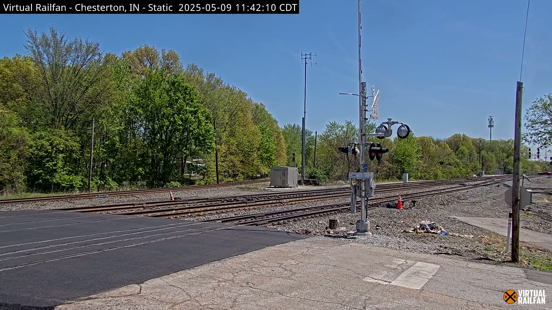 A railroad crossing with traffic signals and new asphalt under a clear blue sky.