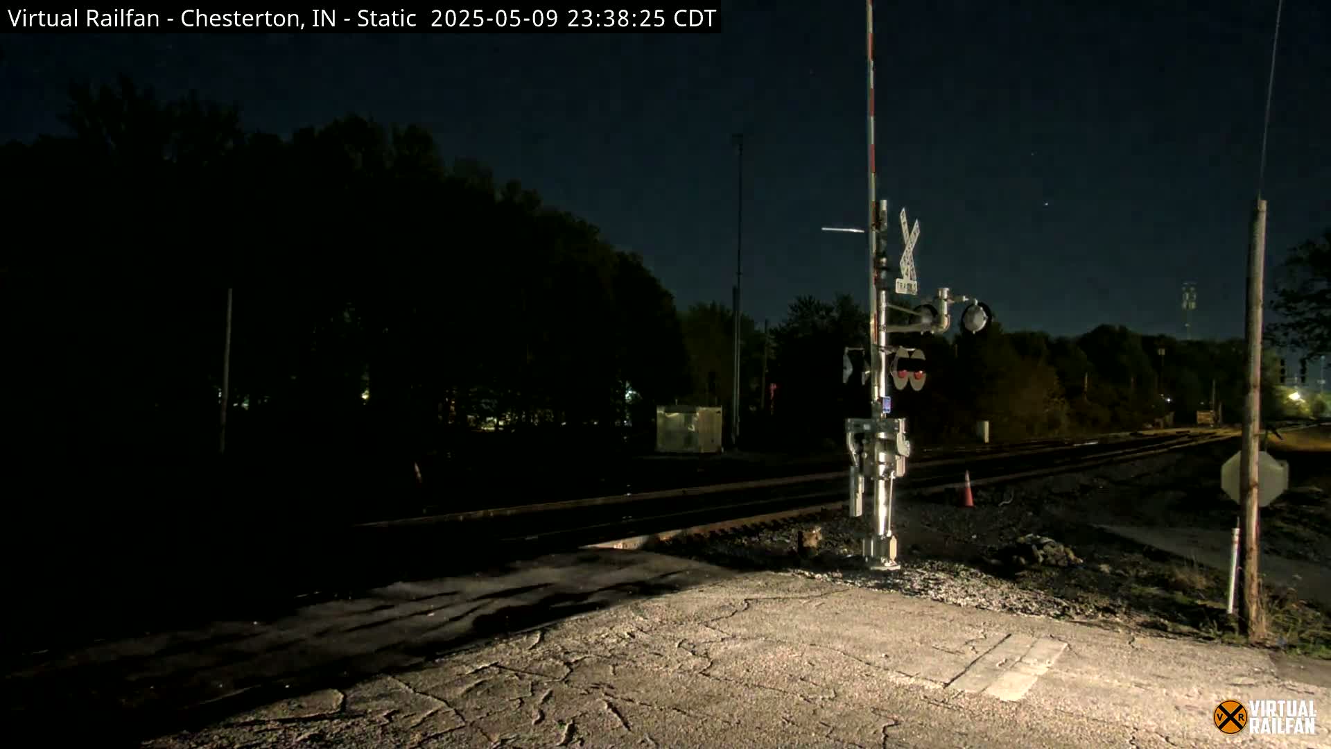 A nighttime view of a railroad crossing with a signal light, under a clear, dark sky.