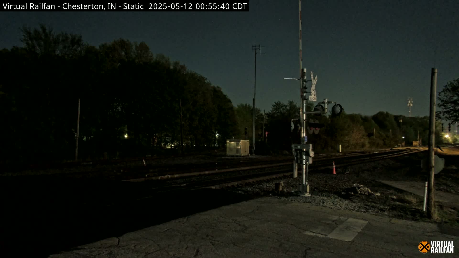 A nighttime view of a railroad crossing with a signal, surrounded by dark trees under a clear night sky.