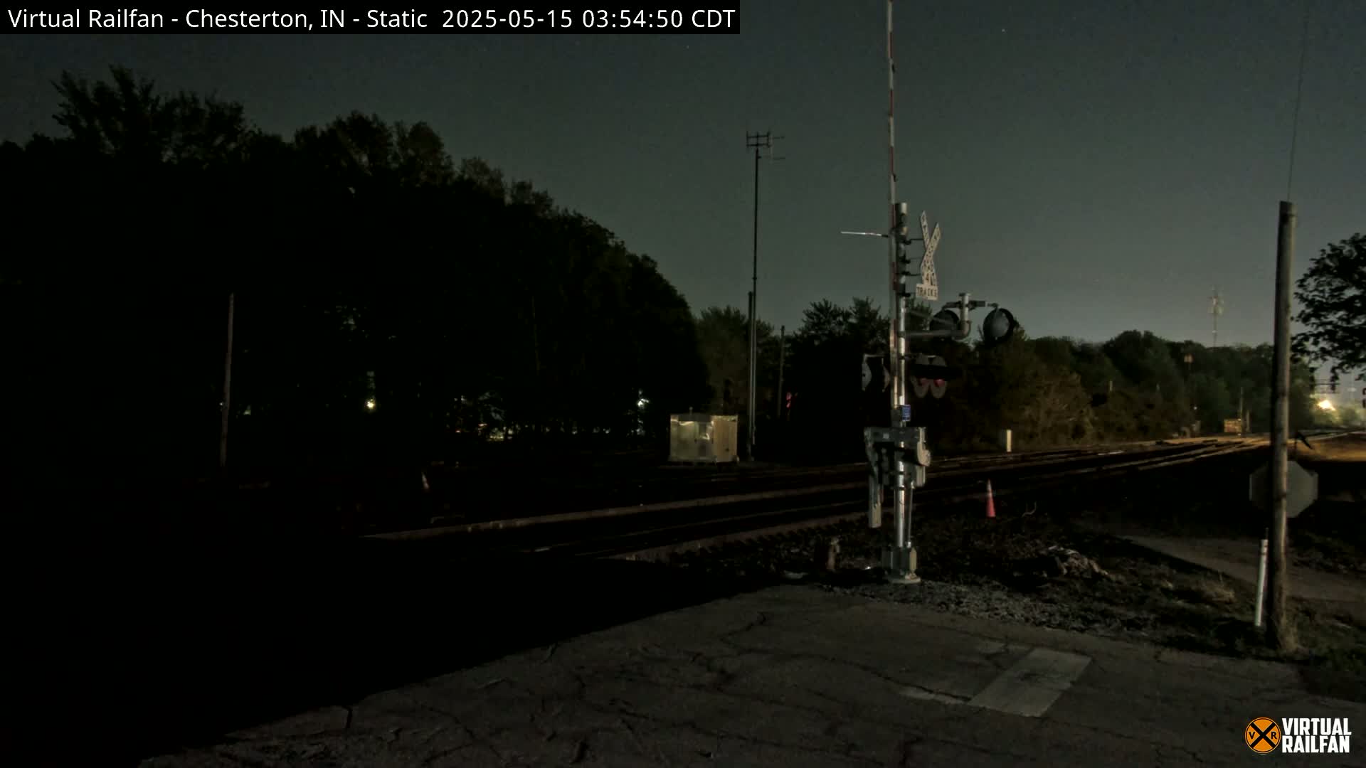 A nighttime view of railroad tracks and crossing signals under a dark sky.