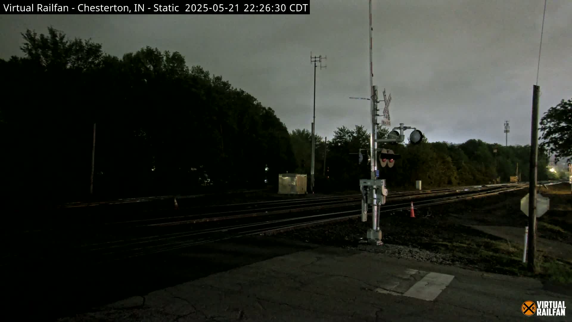 A nighttime view of a railroad crossing with train signals under an overcast sky.