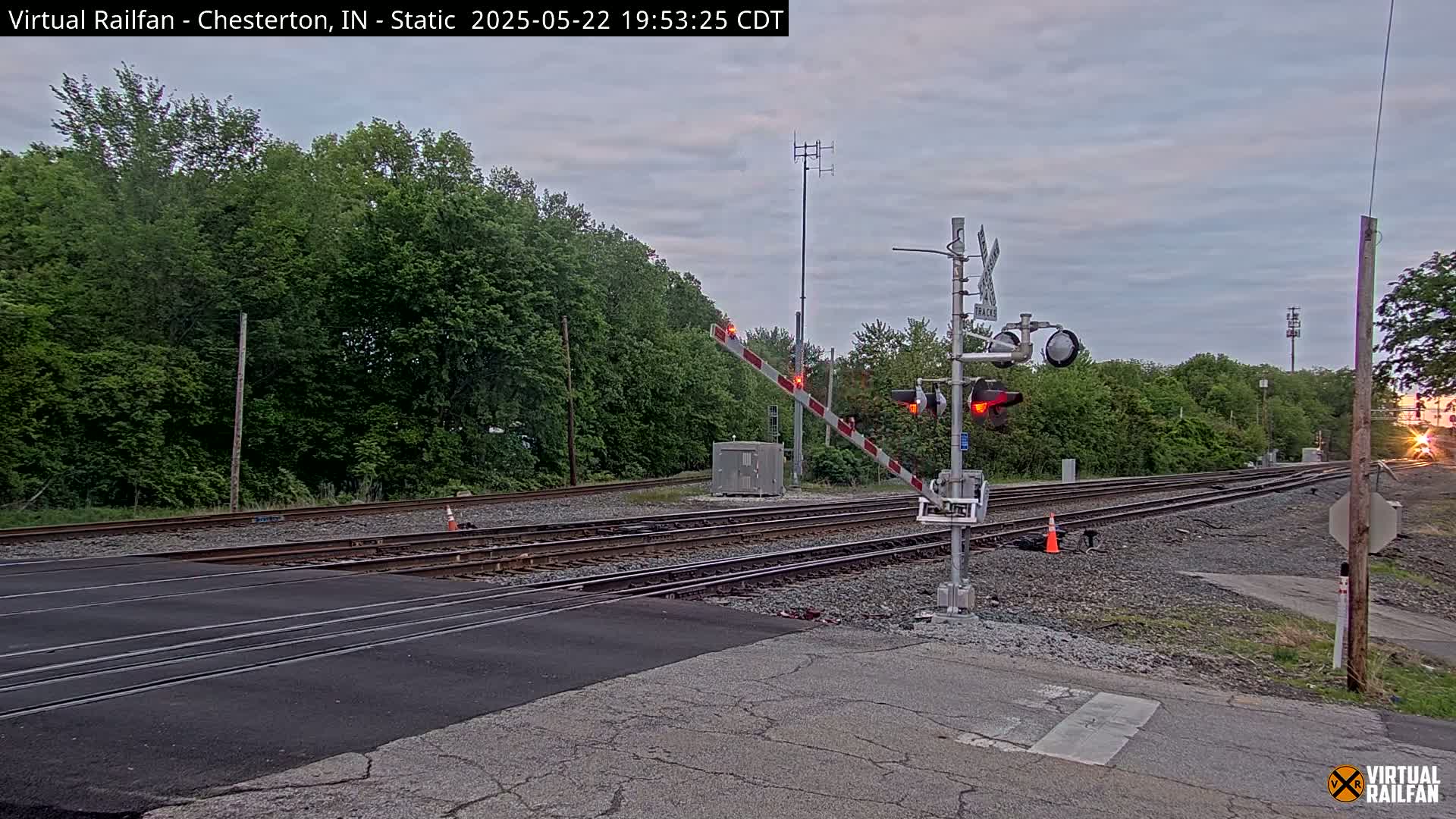 A railroad crossing with its gates down, under an overcast sky, shows a train approaching in the distance.