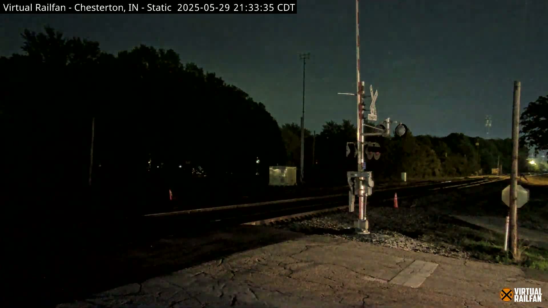 A nighttime view of a railroad crossing with train signals and dark trees in the background under a clear, dark sky.