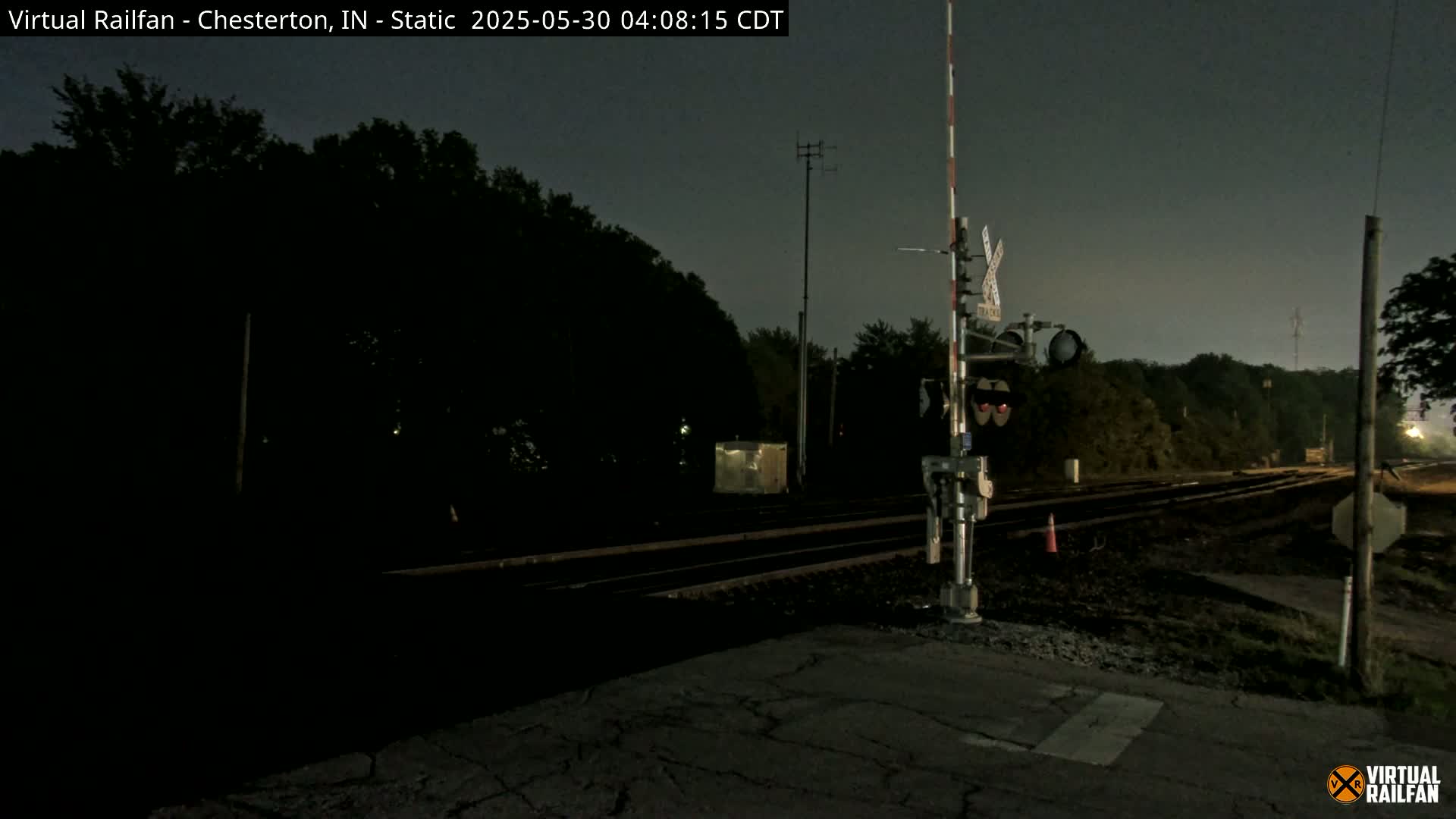 A nighttime view of a railroad crossing with train tracks extending into the dark distance under a mostly clear sky.