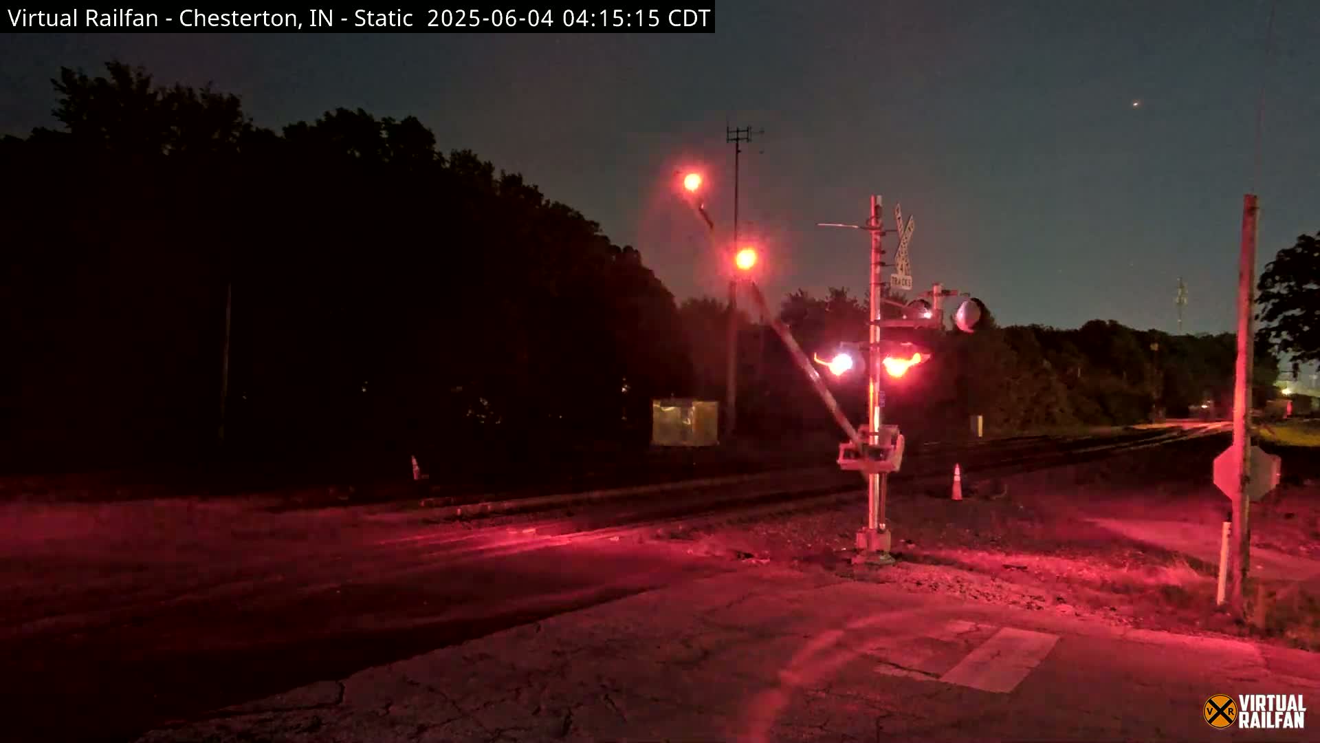 At night, a railroad crossing shows red flashing lights illuminating the area.